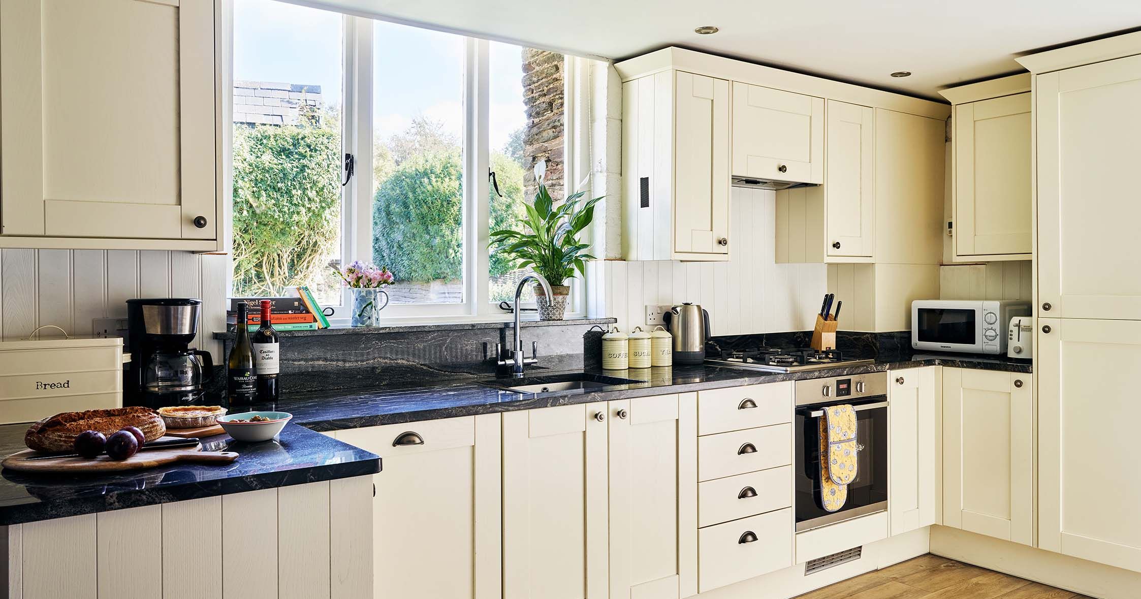 Kitchen in the Granary at Flear Farm Cottages, with cream shaker units, black worktops, large window, and fresh bread and wine on the counter.
