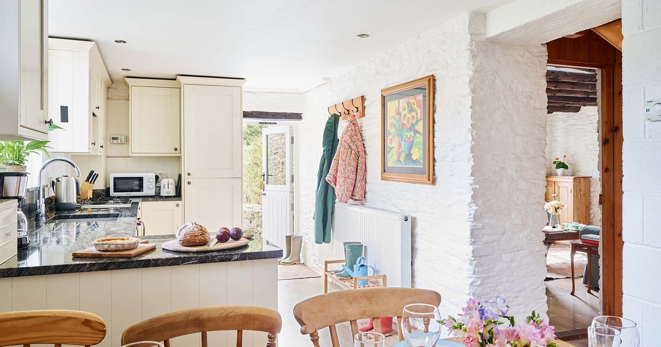 View from the Granary kitchen-diner through to the living room at Flear Farm Cottages, with set dining table, rustic beams, and whitewashed walls.