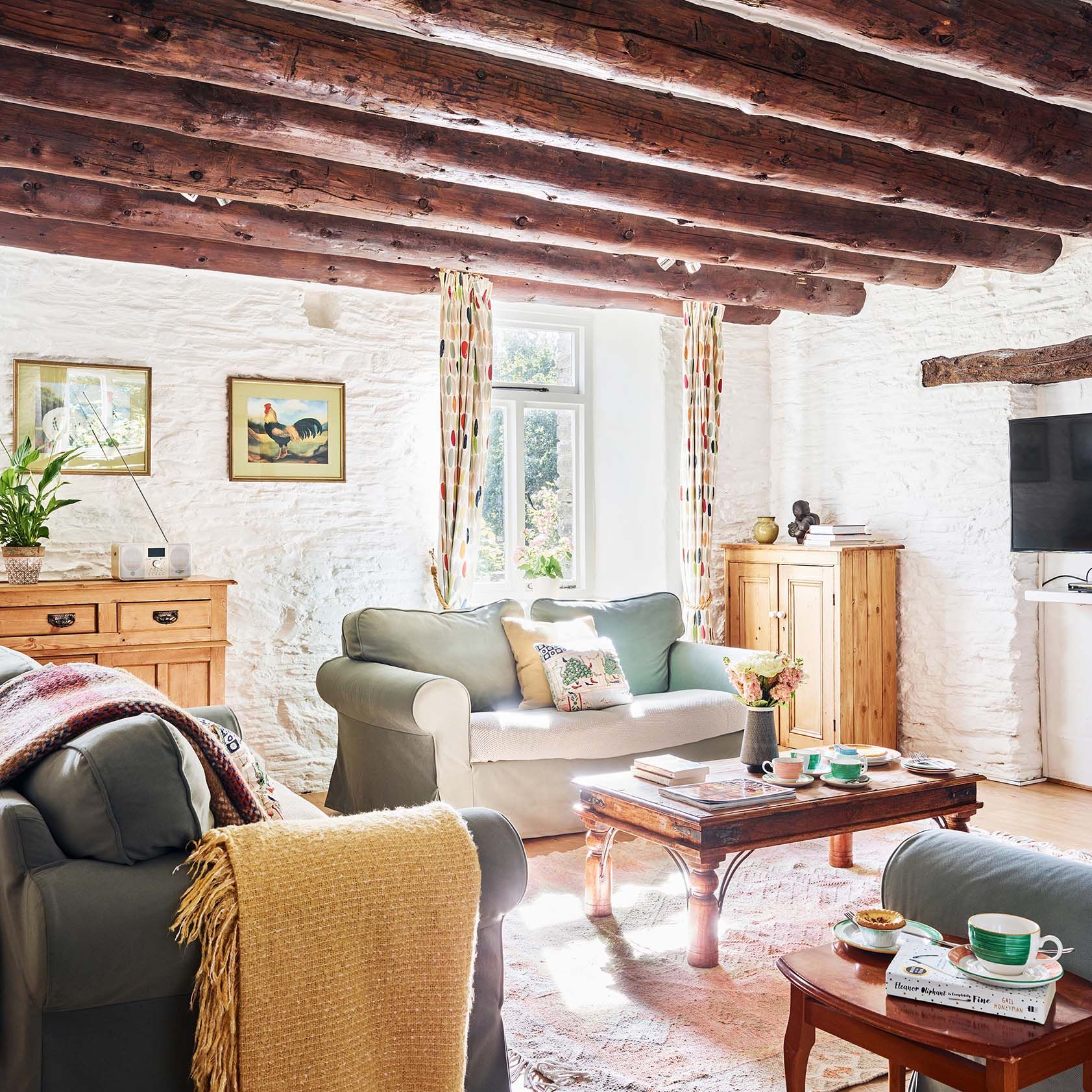 Portrait view of the Granary’s living room at Flear Farm Cottages, with exposed beams, soft seating, rustic furnishings, and sunlight streaming in.