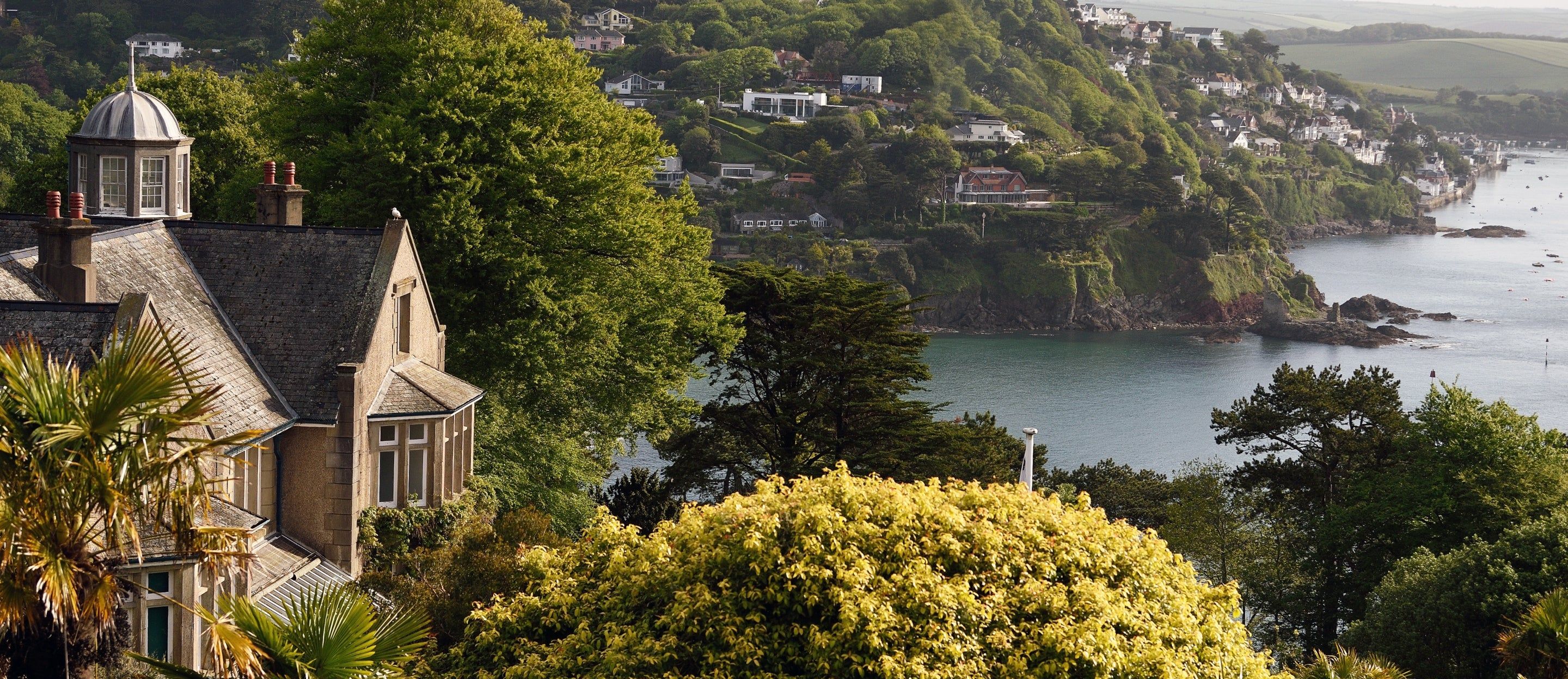 Overbeck’s Garden in South Devon featuring dense greenery, palm trees, and a coastal view across the water to hillside villages.