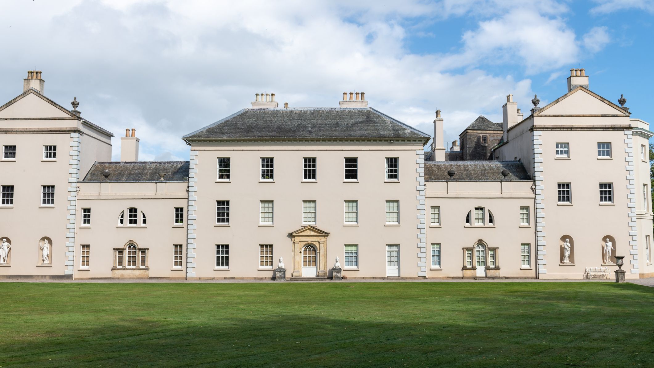 Front facade of Saltram House in Plymouth, a grand pale-stone mansion with symmetrical wings, statues in niches and a wide lawn.