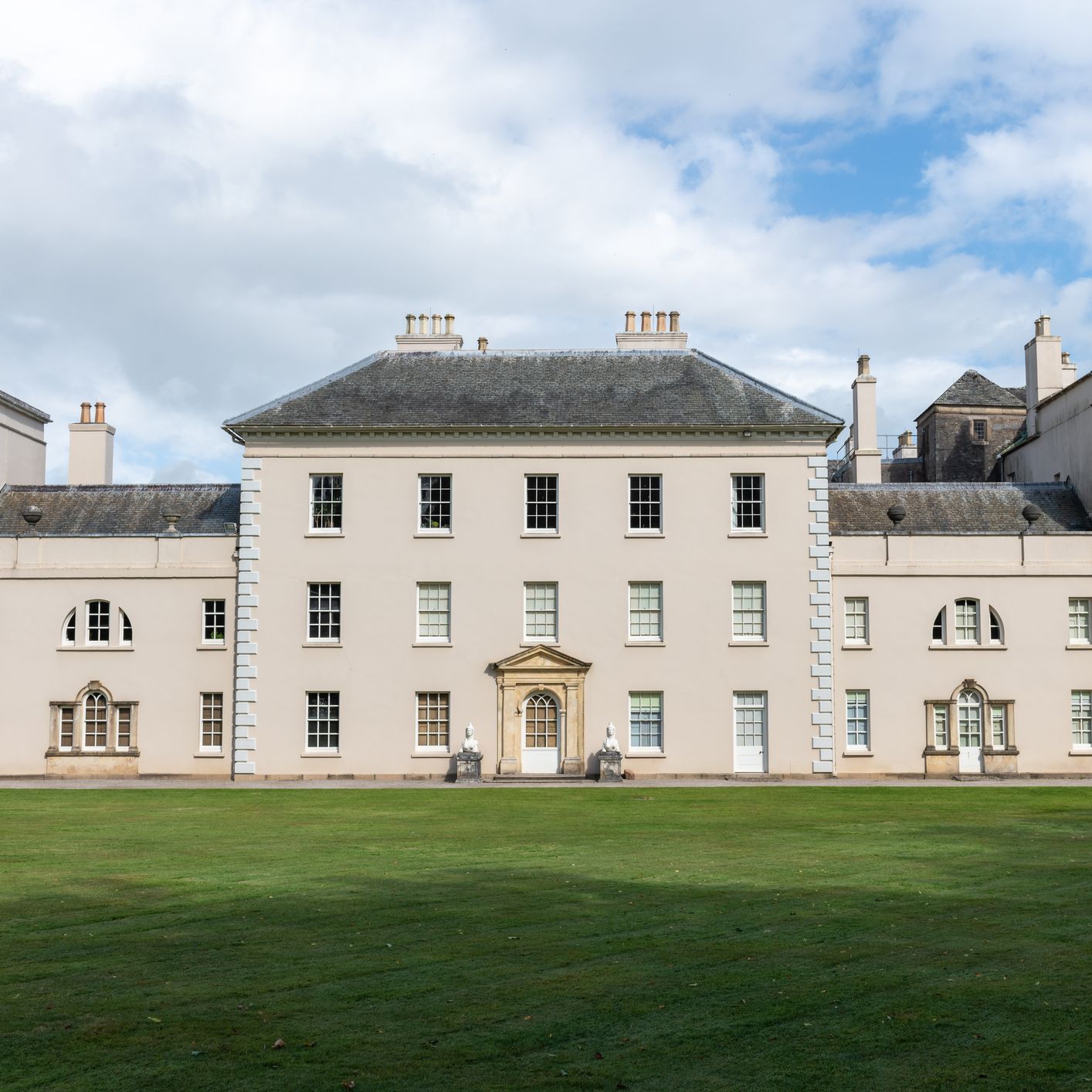 Front facade of Saltram House in Plymouth, a grand pale-stone mansion with symmetrical wings, statues in niches and a wide lawn.