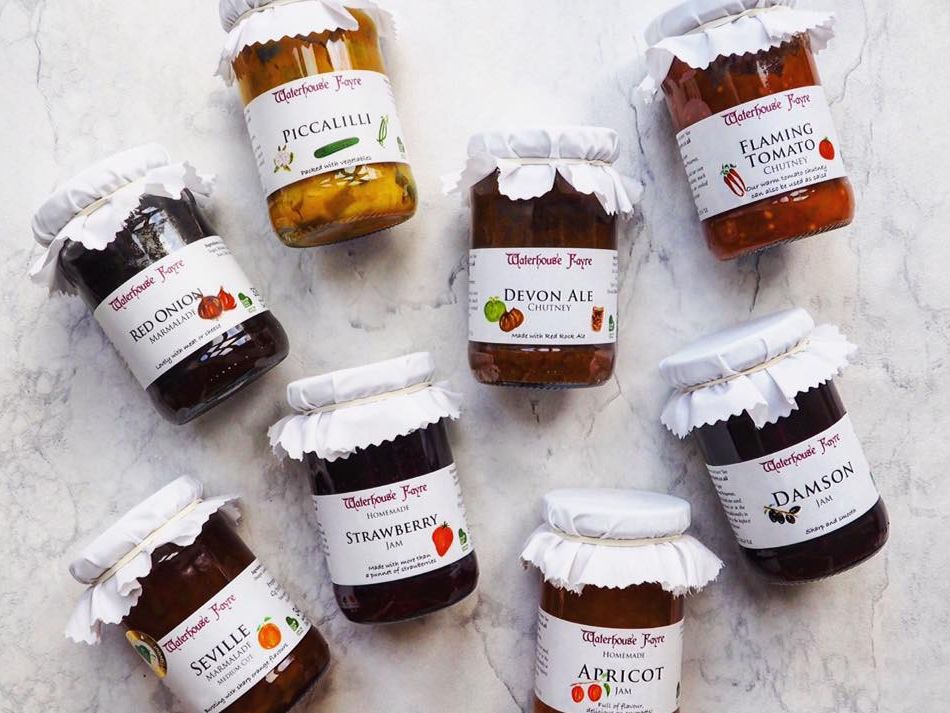 Assorted jars of Waterhouse Fayre jams, marmalades, chutneys and piccalilli on a light marble surface