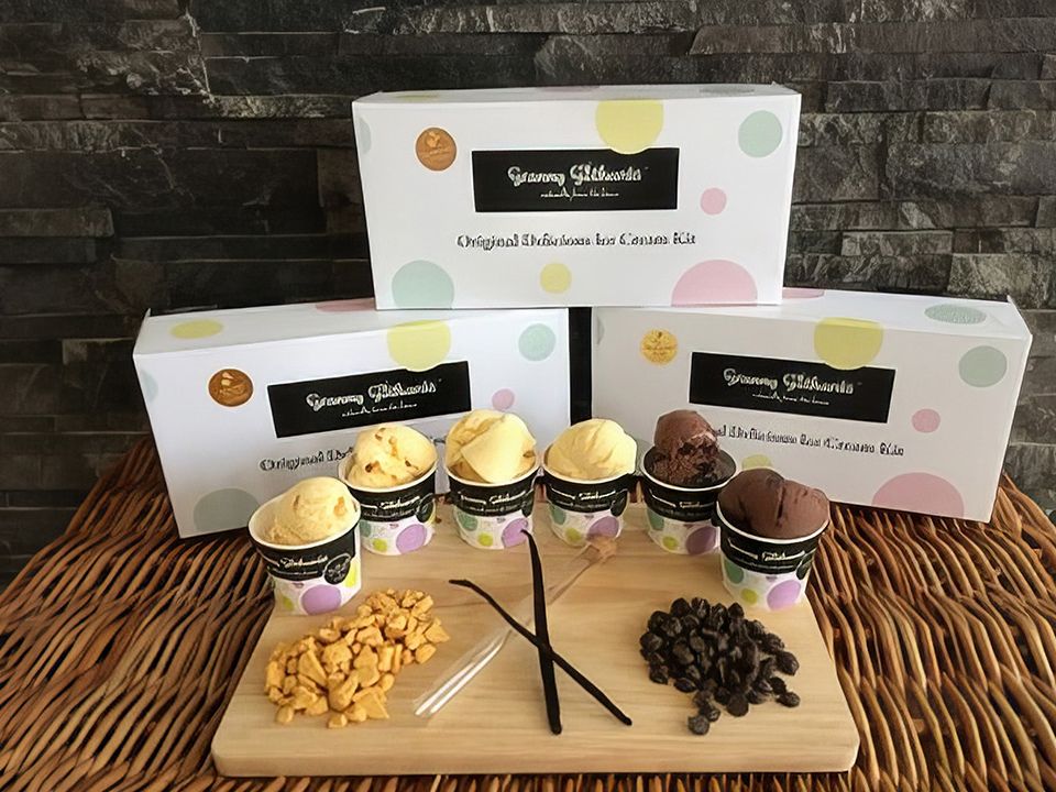 Assorted ice cream tubs with gift boxes, toppings and vanilla pods on a wooden board