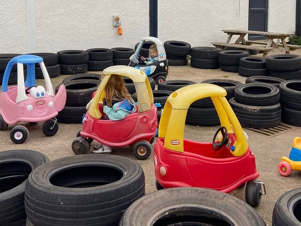 Children driving Little Tikes toy cars around a tyre-lined race track outdoors