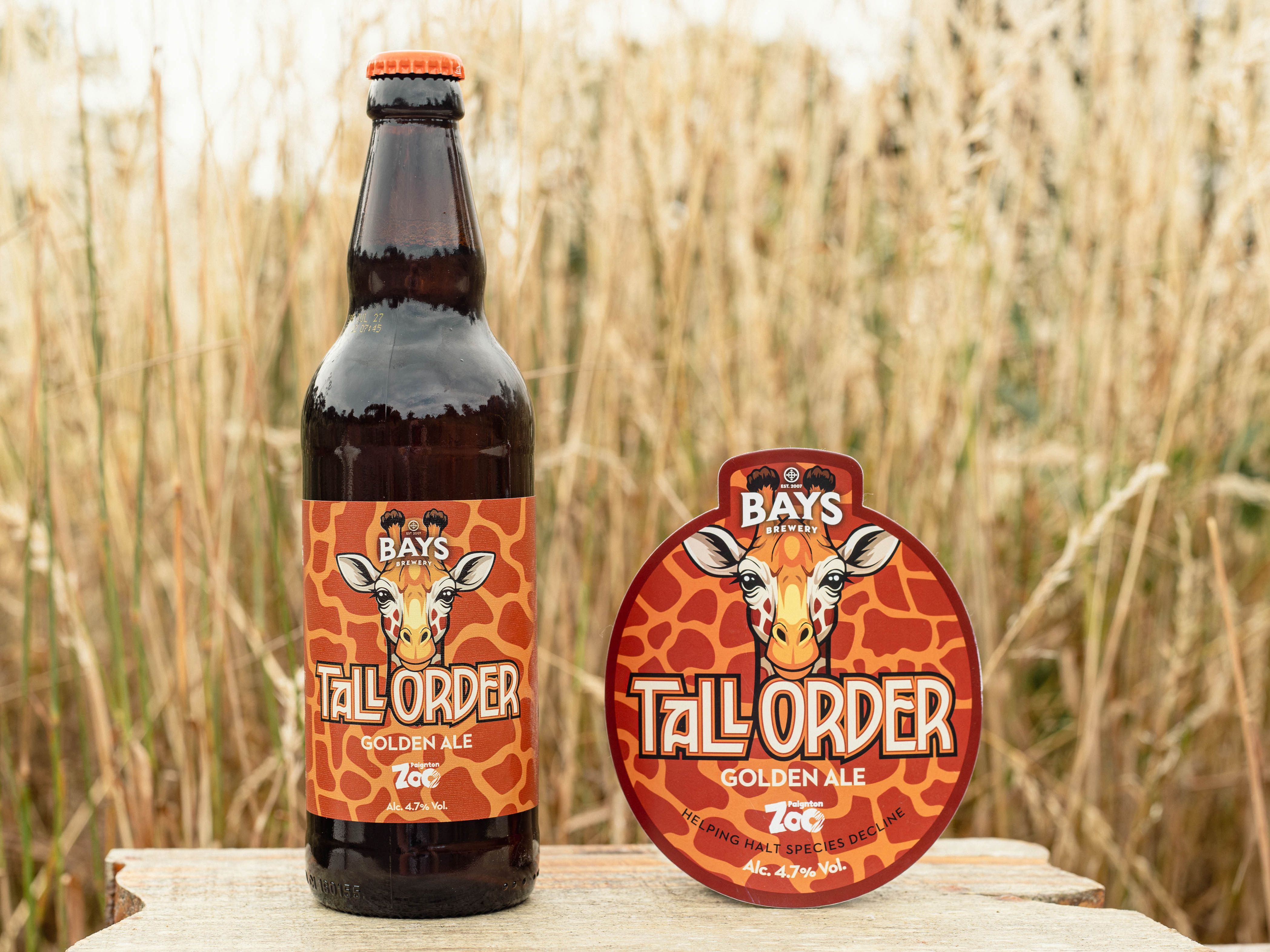 A colourful bottle of Bays Brewery Tall Order charity ale featuring a picture of a giraffe next to the beer tap cover