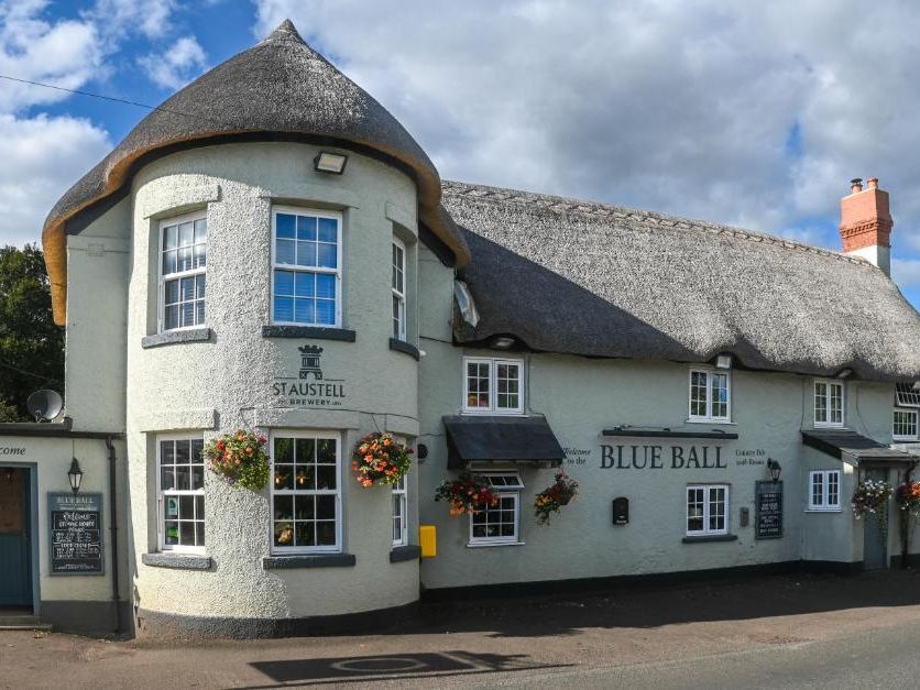 Image of the front of a thatched pub with floral displays - The Blue Ball Inn at Sandygate Exeter