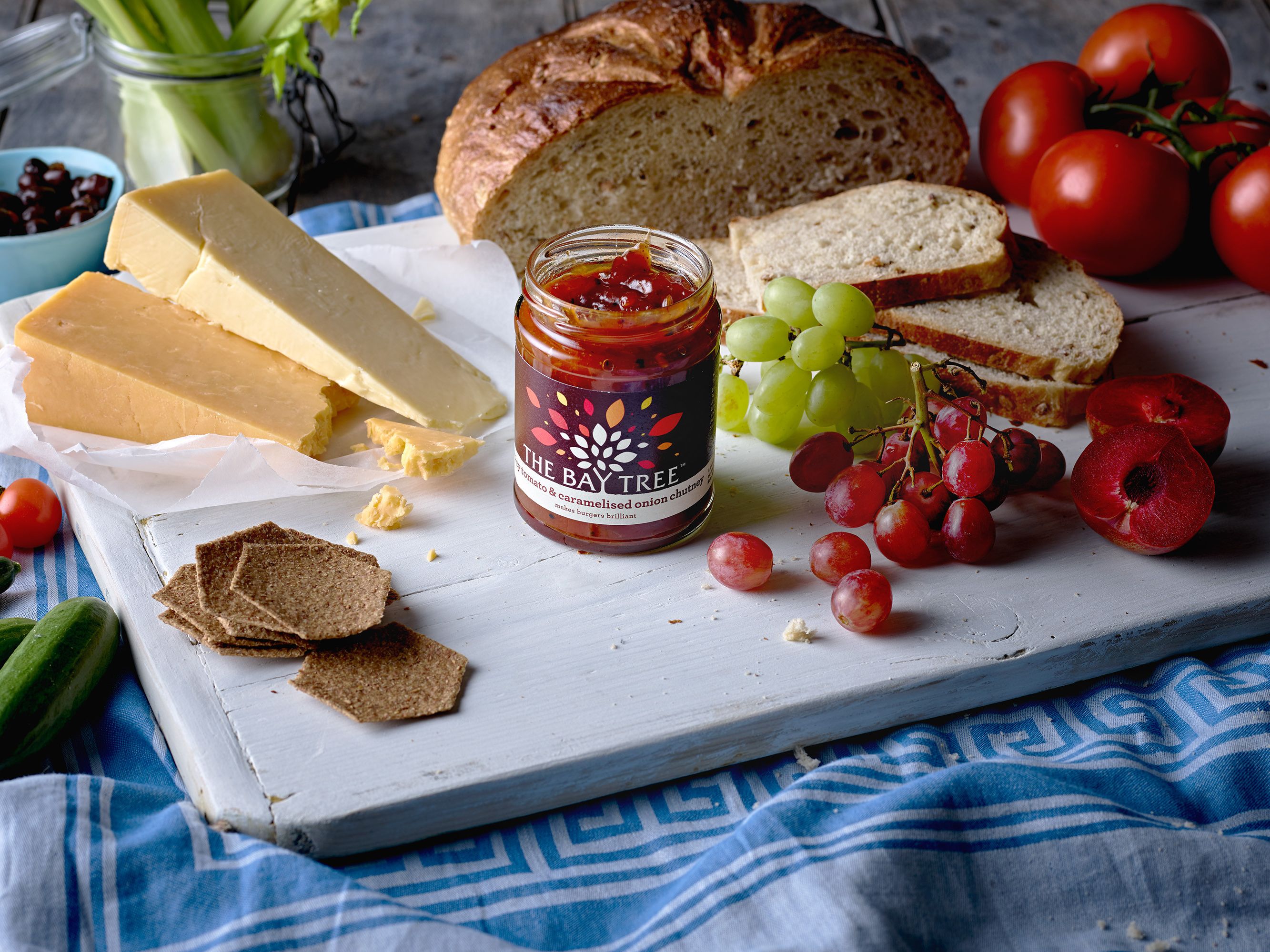 The Bay Tree Food Co. open jar at the centre of a cheeseboard with bread, grapes and crackers