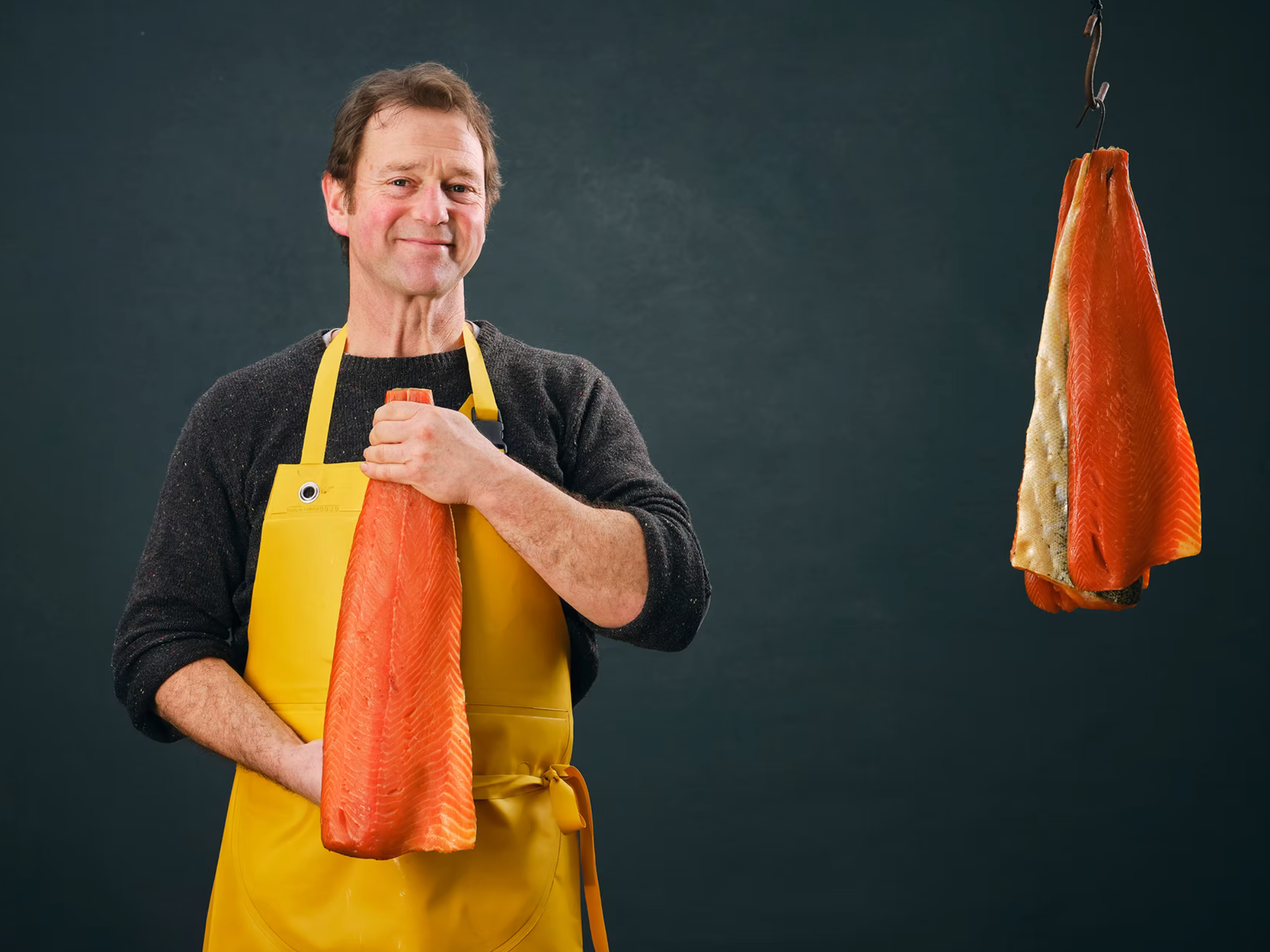 Blakewell Smokehouse owner John Nickell holding a side of smoked salmon wearing a yellow apron