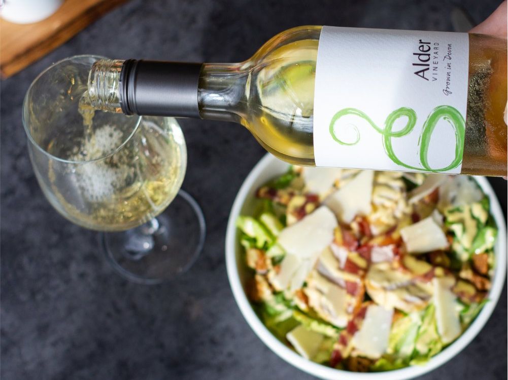 Alder Vineyard Madeleine Angevine bottle being pured into a wine glass alongside a plate of food