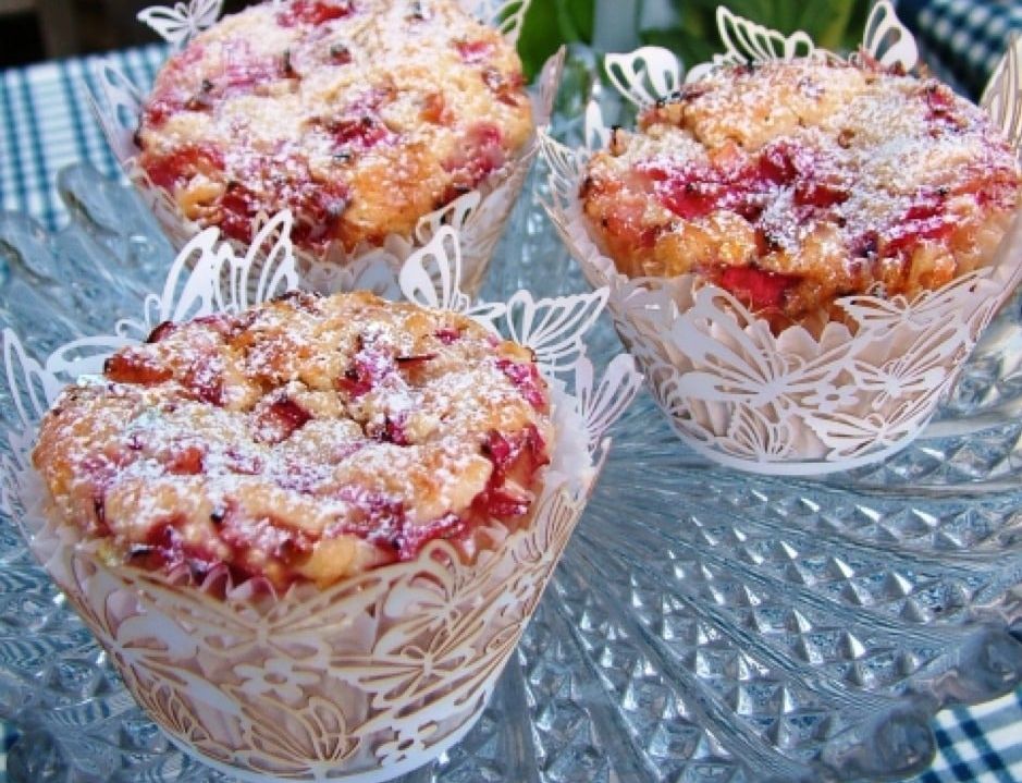 Rhubarb & custard muffins topped with powdered sugar are displayed on a glass cake stand.