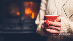 A person warming up by the fire with a hot drink.