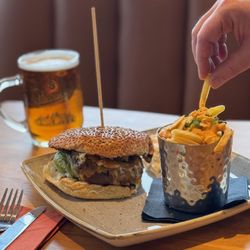 Someone pinching a chip from a plate with a burger and chips on it, with a beer in the background.