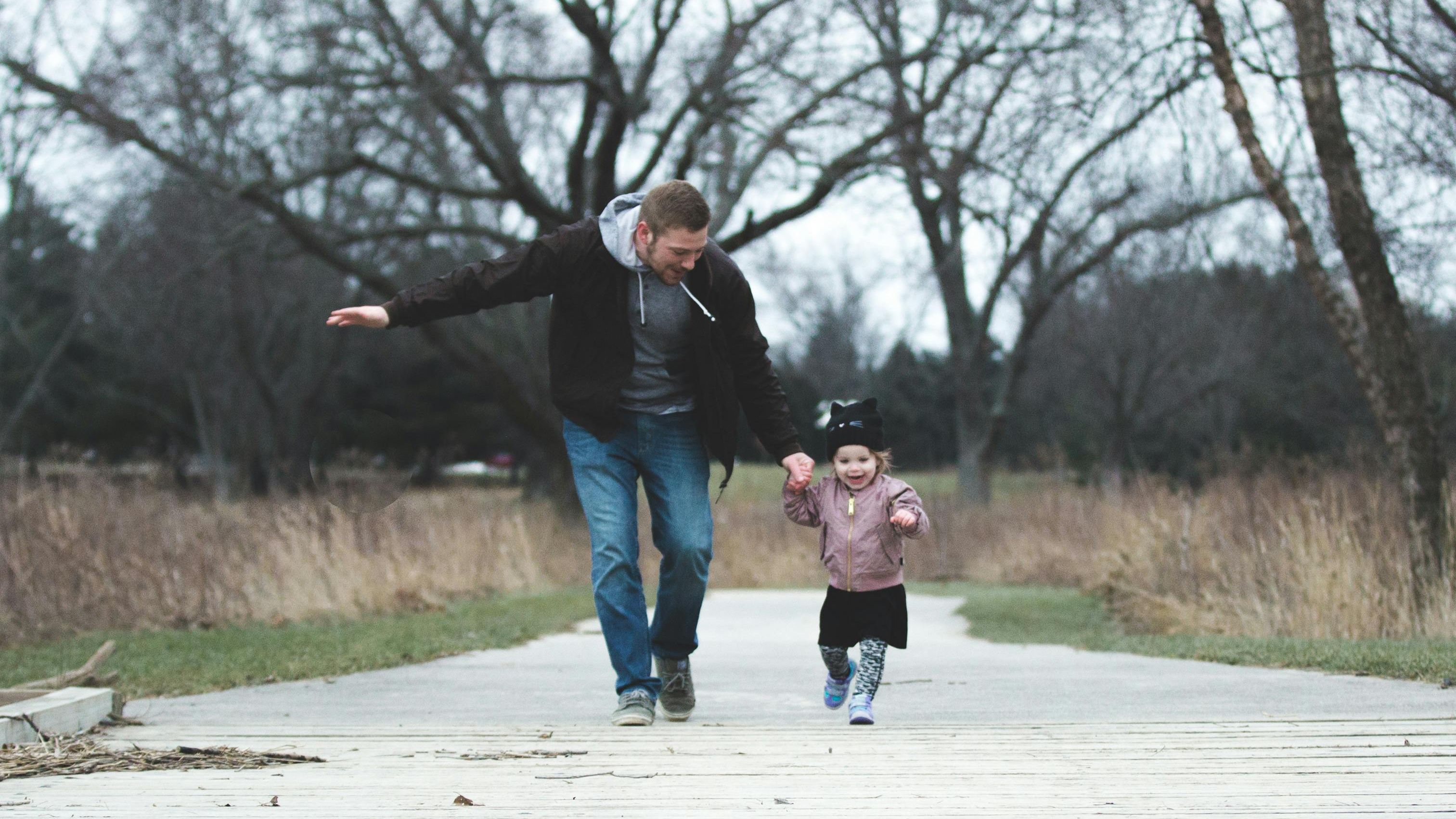 Father and daughter joyfully running hand in hand on a park path—capturing a heartwarming moment and one of many simple Father’s Day activity ideas.