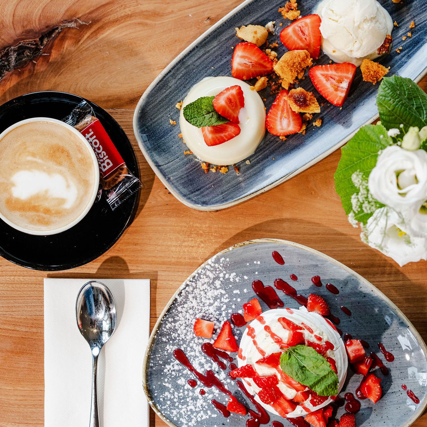 Table with coffee, desserts topped with strawberries, a glass of white wine, and a vase of white flowers.