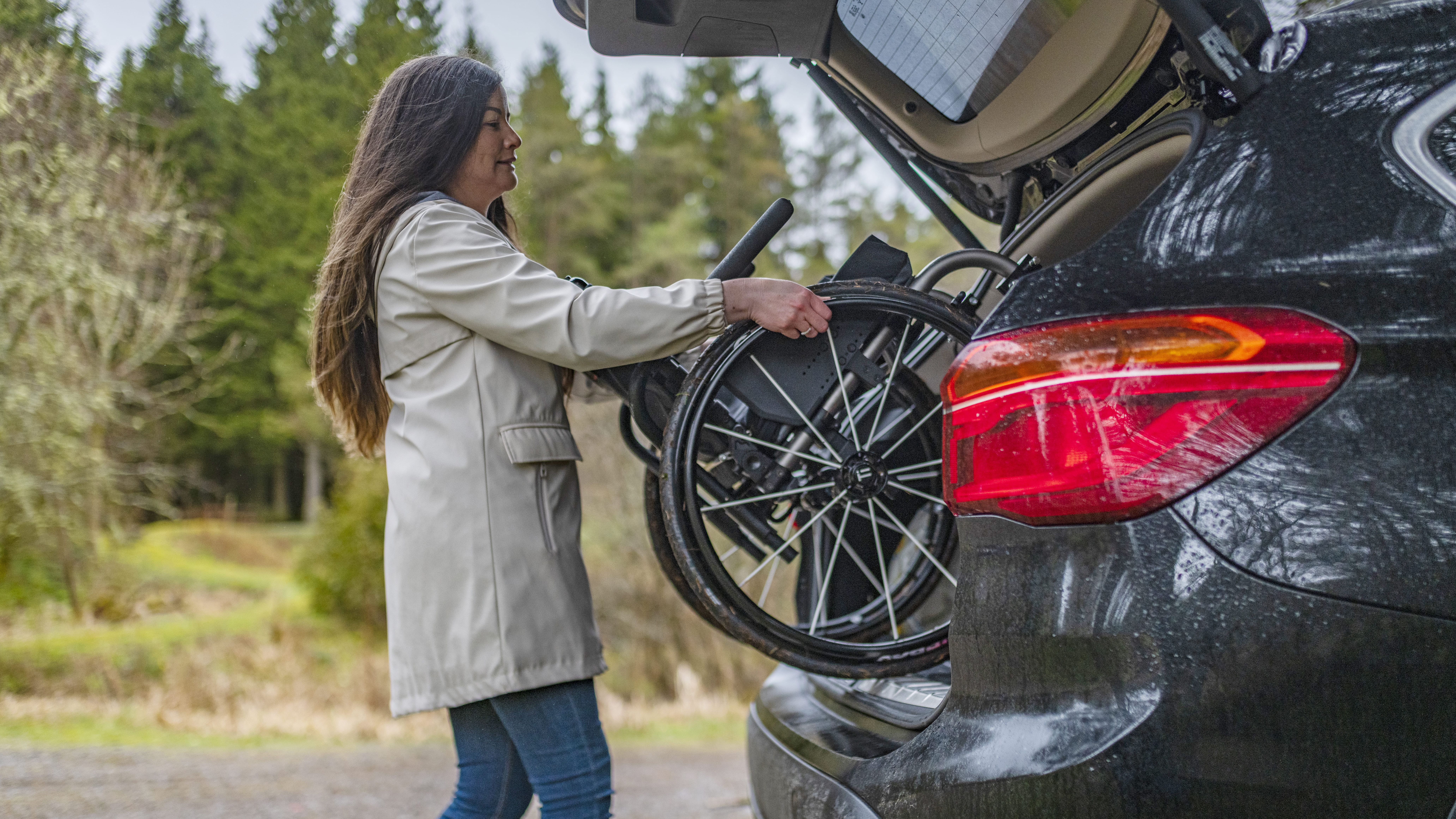 Woman loading a wheelchair into the trunk of a car in a forest setting