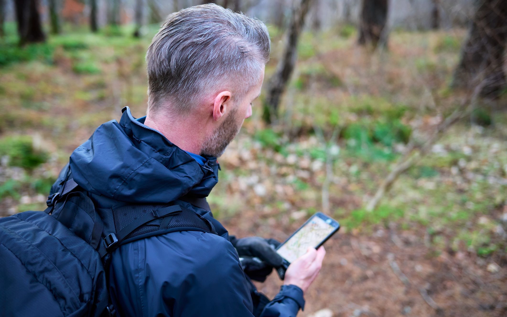 Hiker with a backpack checking a smartphone map in a wooded area.