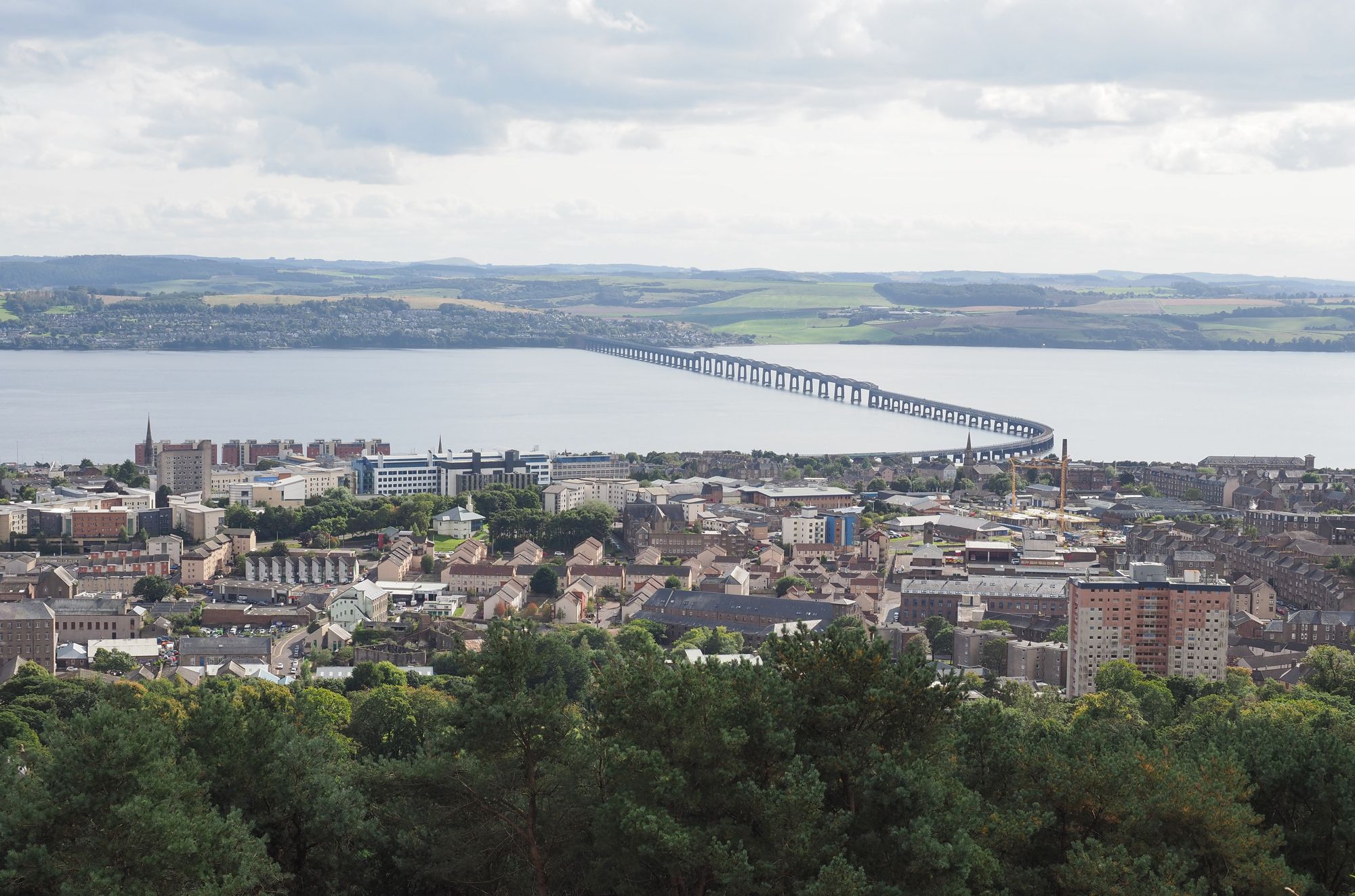 View of Dundee from Law Hill, with the Tay Road Bridge stretching across the River Tay under a cloudy sky.