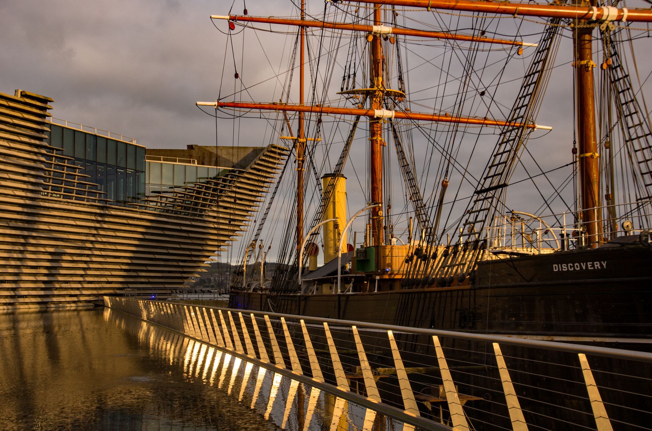 Historic ship named Discovery docked beside the modern architecture of the V&A Dundee museum.