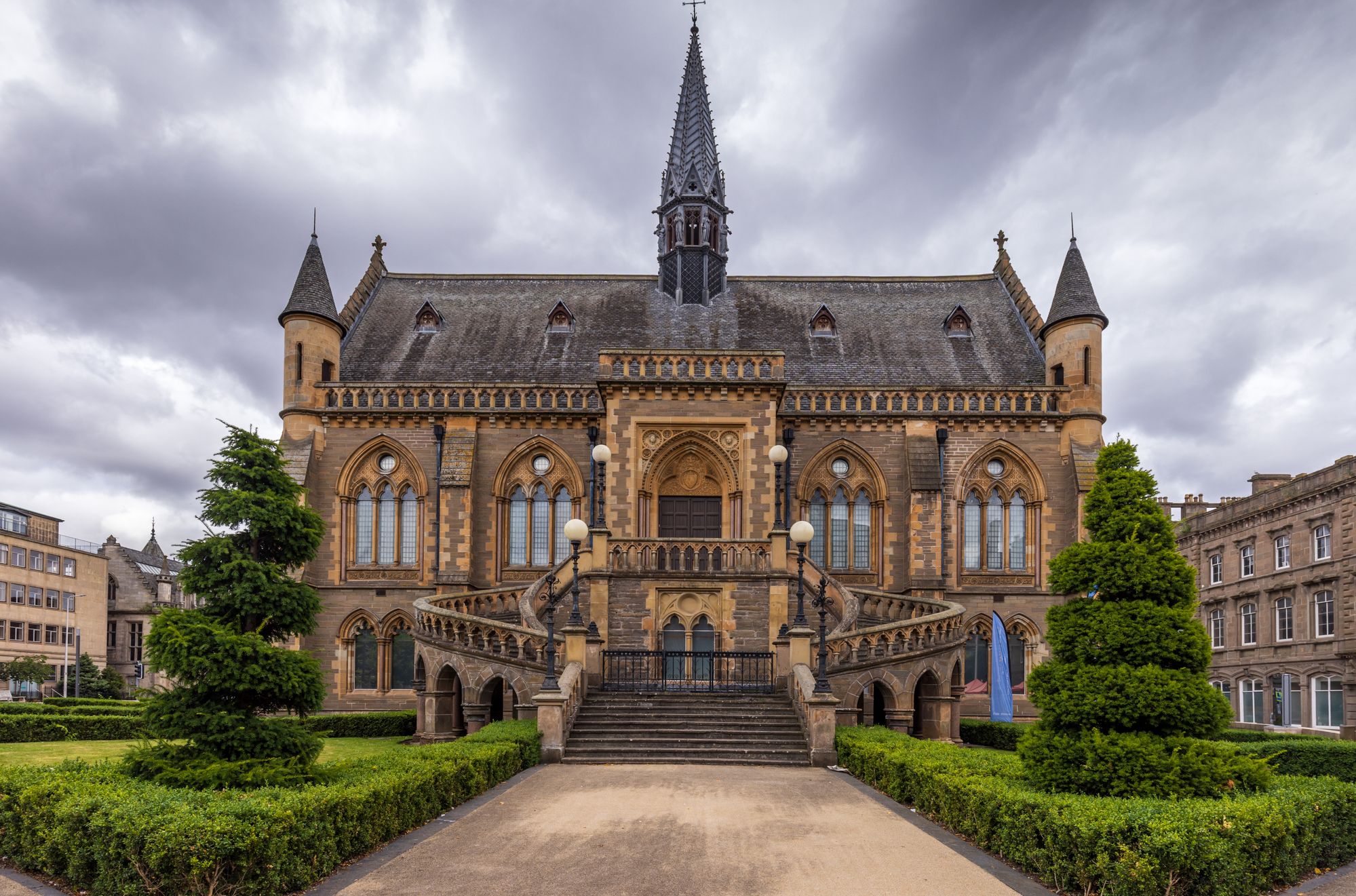 Historic stone building with arched windows, two towers, a central spire, and grand symmetrical staircases.