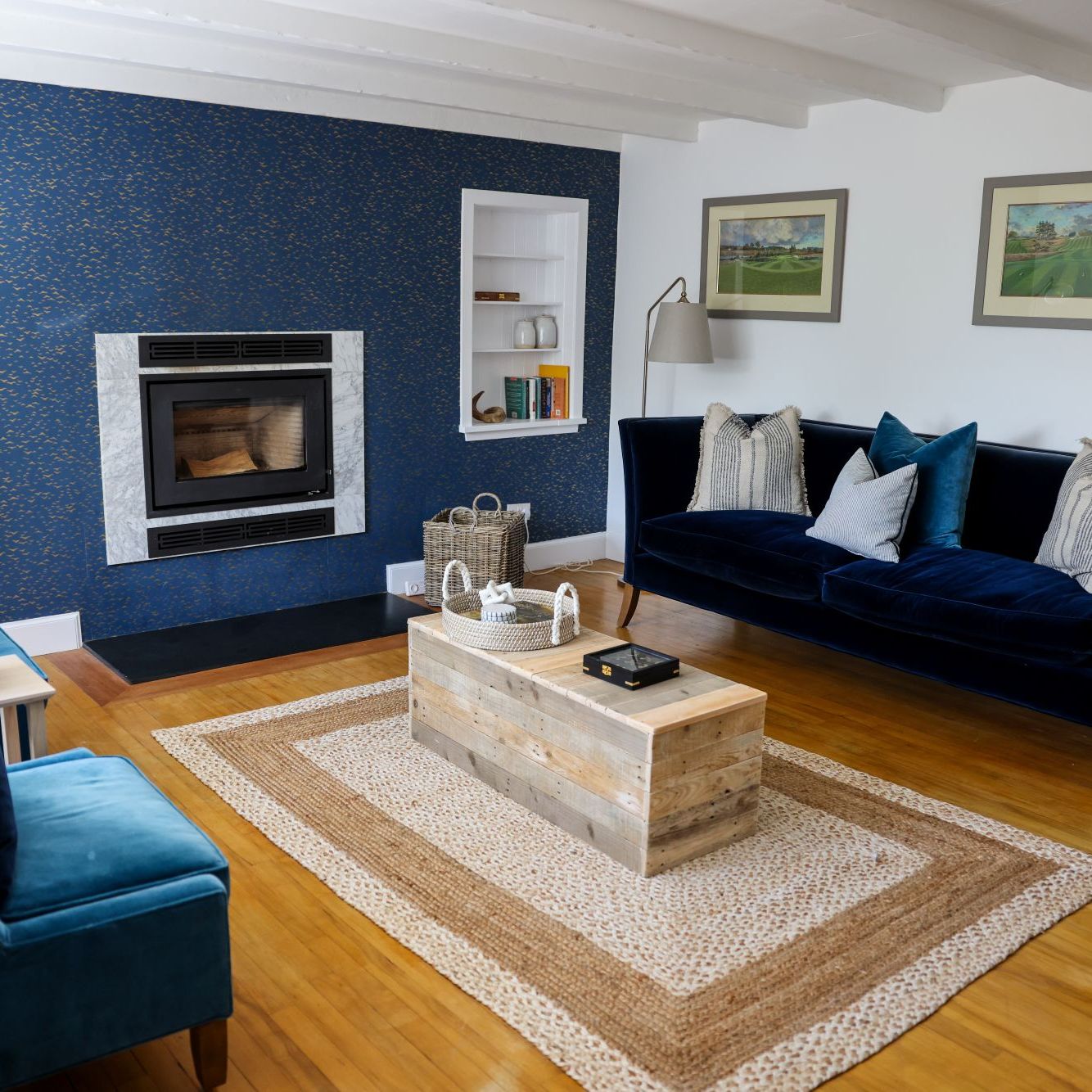 Modern living room with blue accent wall, wood fireplace, navy blue velvet furniture, and wooden coffee table.