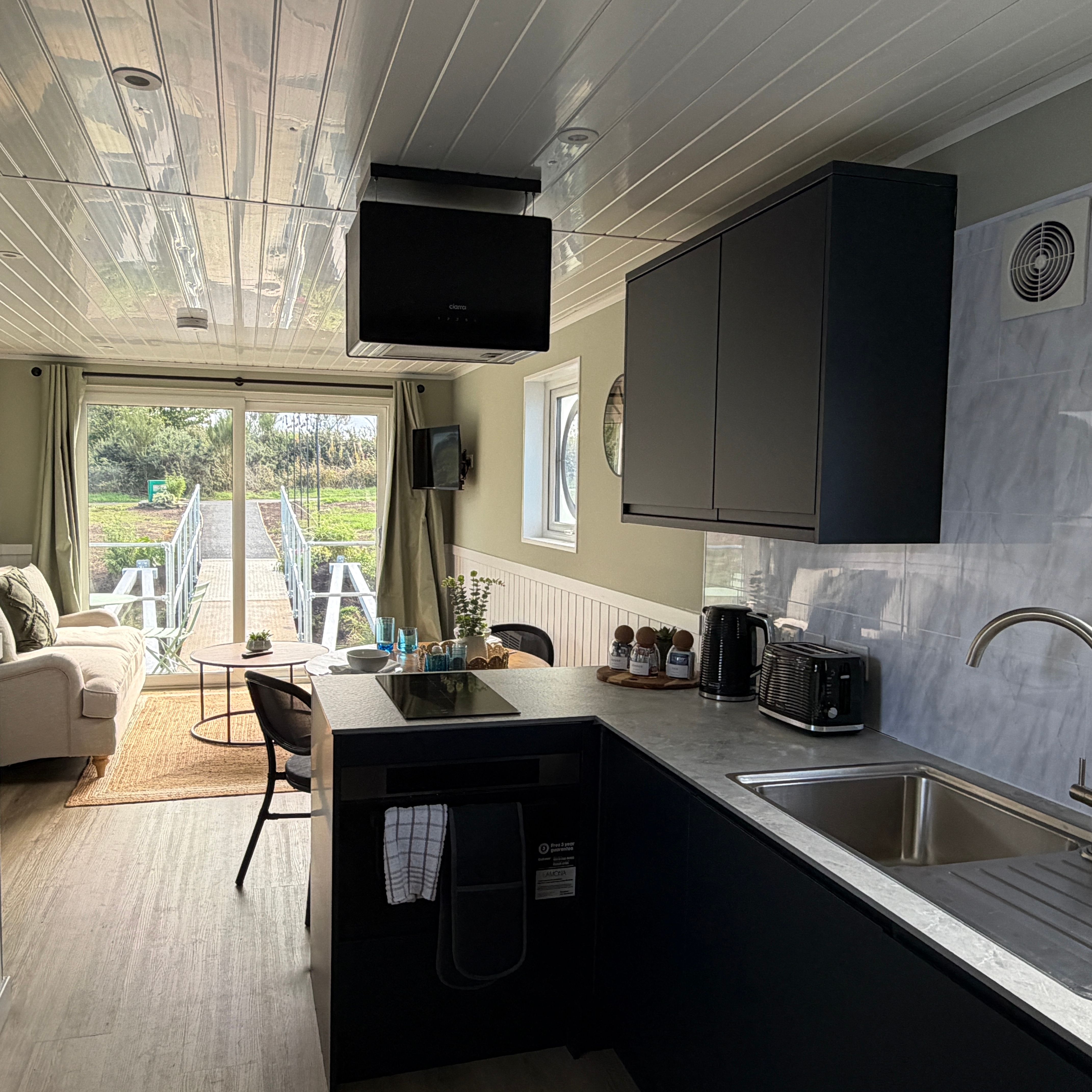 Modern tiny house interior with kitchen and living area, featuring a sliding glass door leading to an outdoor deck.
