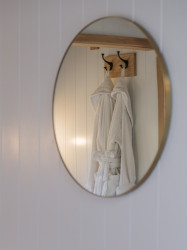 Mirror with reflection of robes hanging on hooks in shepherds hut