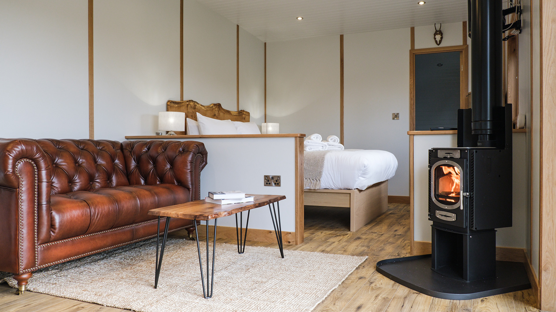 Seating area with log burner and bed in Bankside Bothy