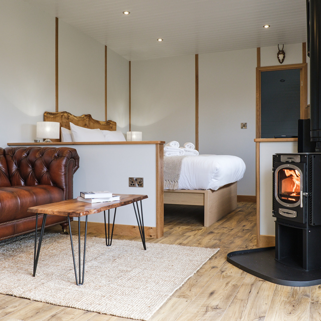 Seating area with log burner and bed in Bankside Bothy