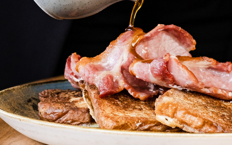 Maple syrup pouring over bacon and pancakes