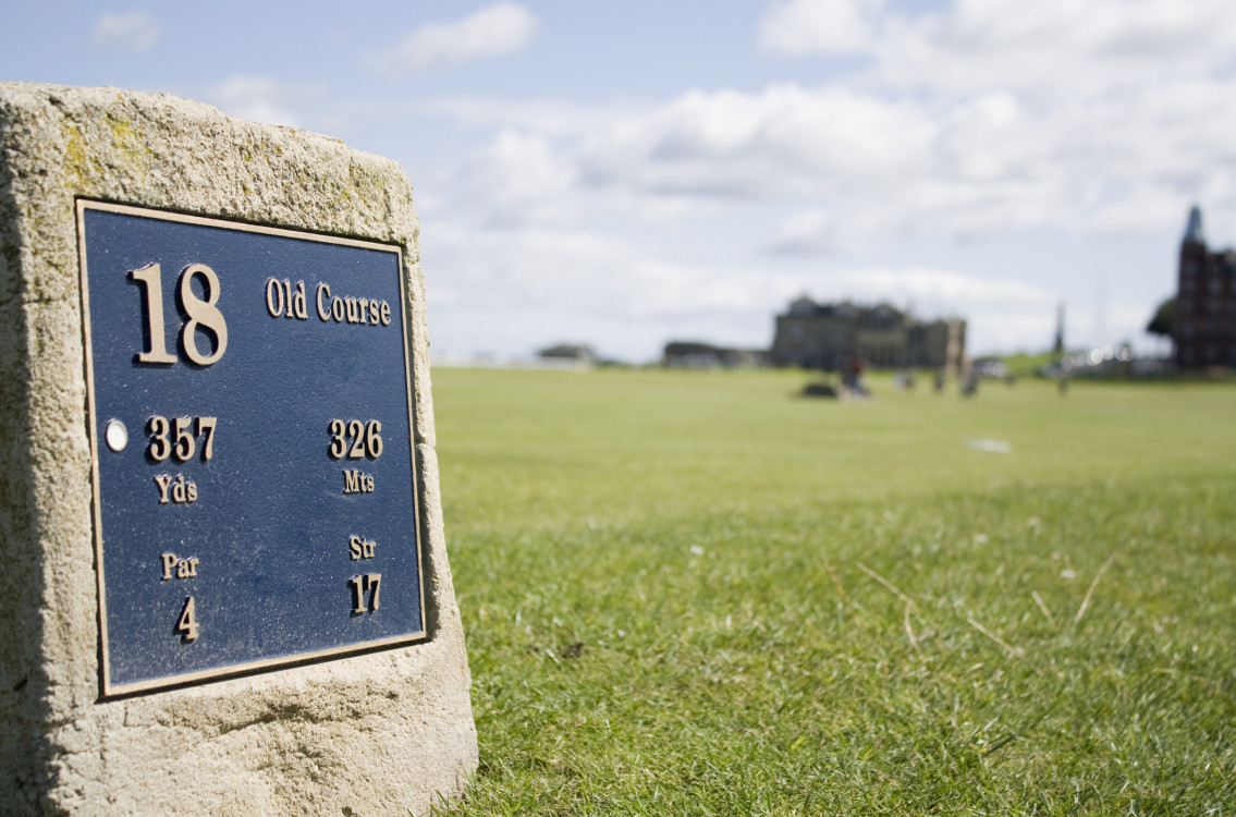 Stone marker for the 18th hole at the Old Course, with a view of the course in the distance.