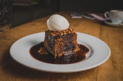 A rich, sticky toffee pudding topped with a scoop of vanilla ice cream, served on a white plate with caramel sauce drizzled around the dessert.