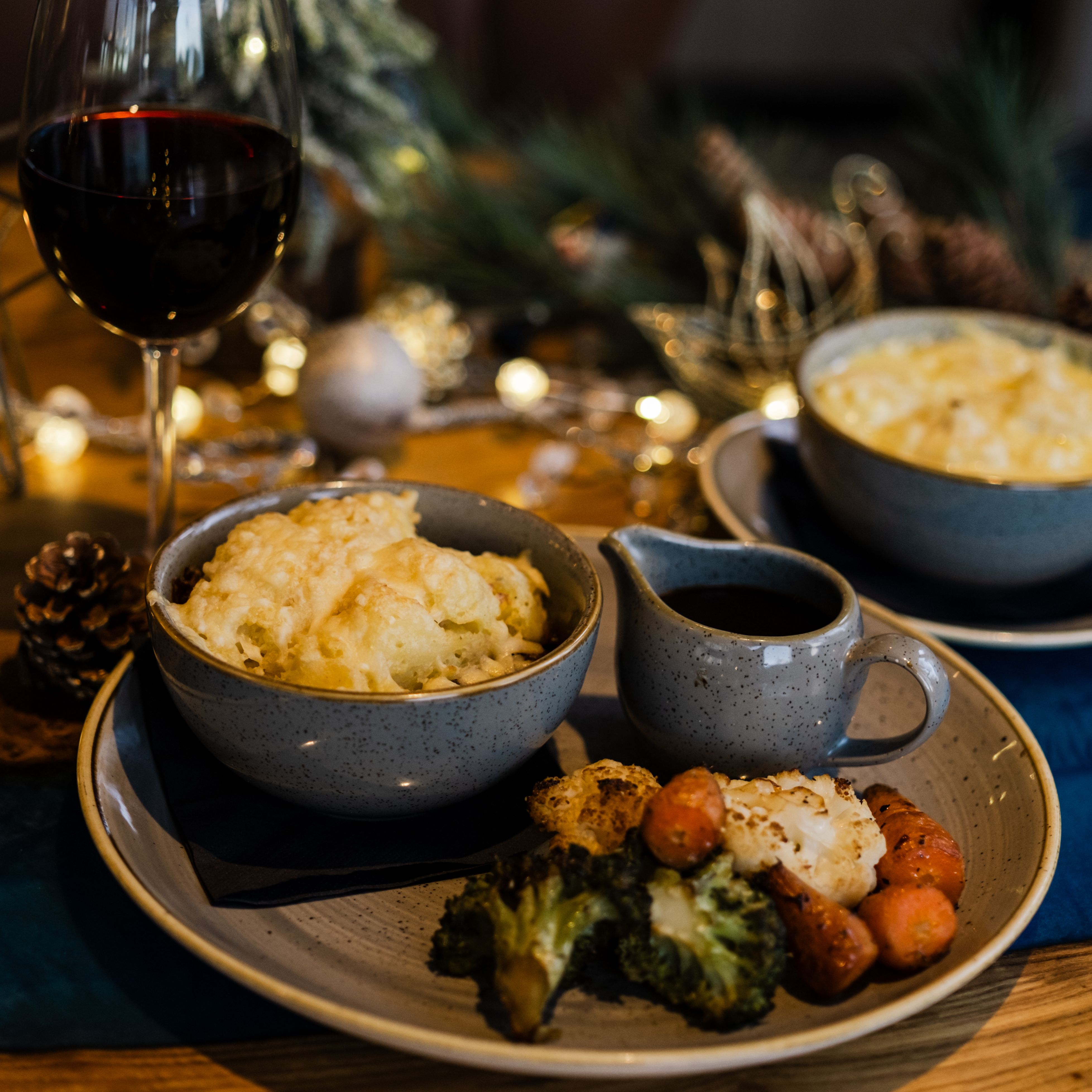 A hearty winter's pie with a glass of red wine, against a backdrop of Christmas twinkling lights.