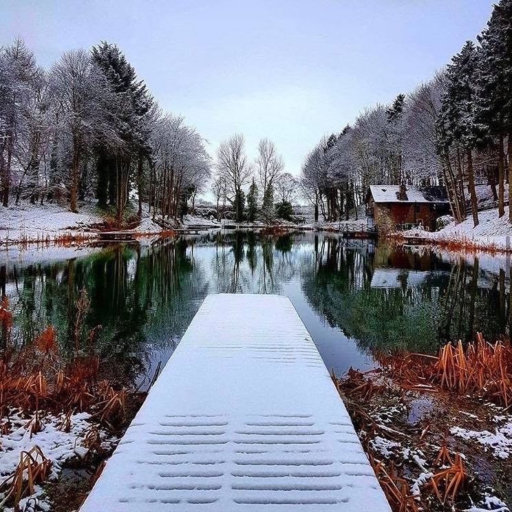 A frosty scene with views from a snow covered fishing pontoon out towards a fishing pond with the Leannan Boathouse.