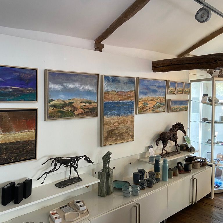 Art gallery wall displaying landscape paintings, ceramic pottery, and horse sculptures