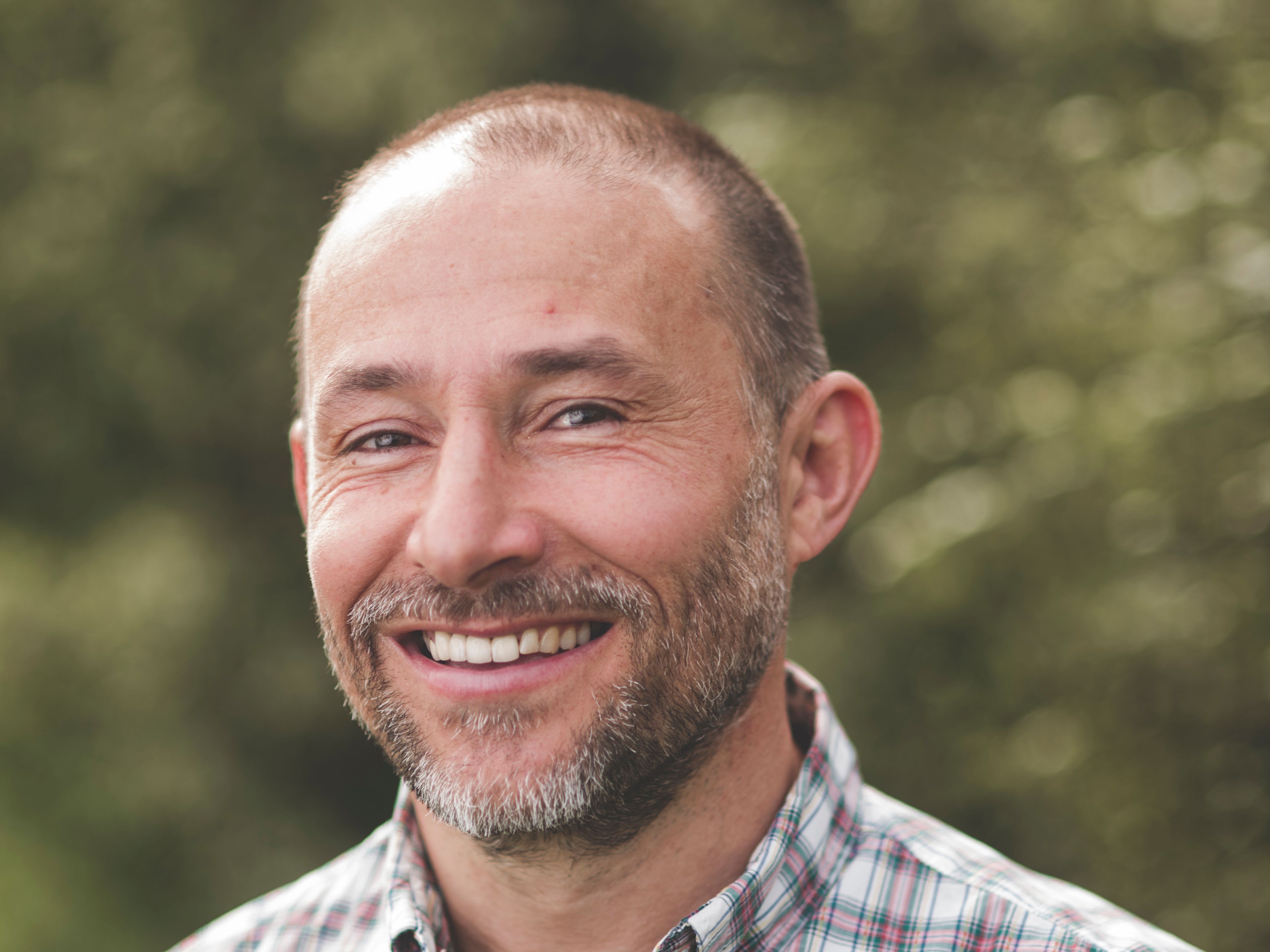 Smiling man with a beard wearing a plaid shirt standing outdoors