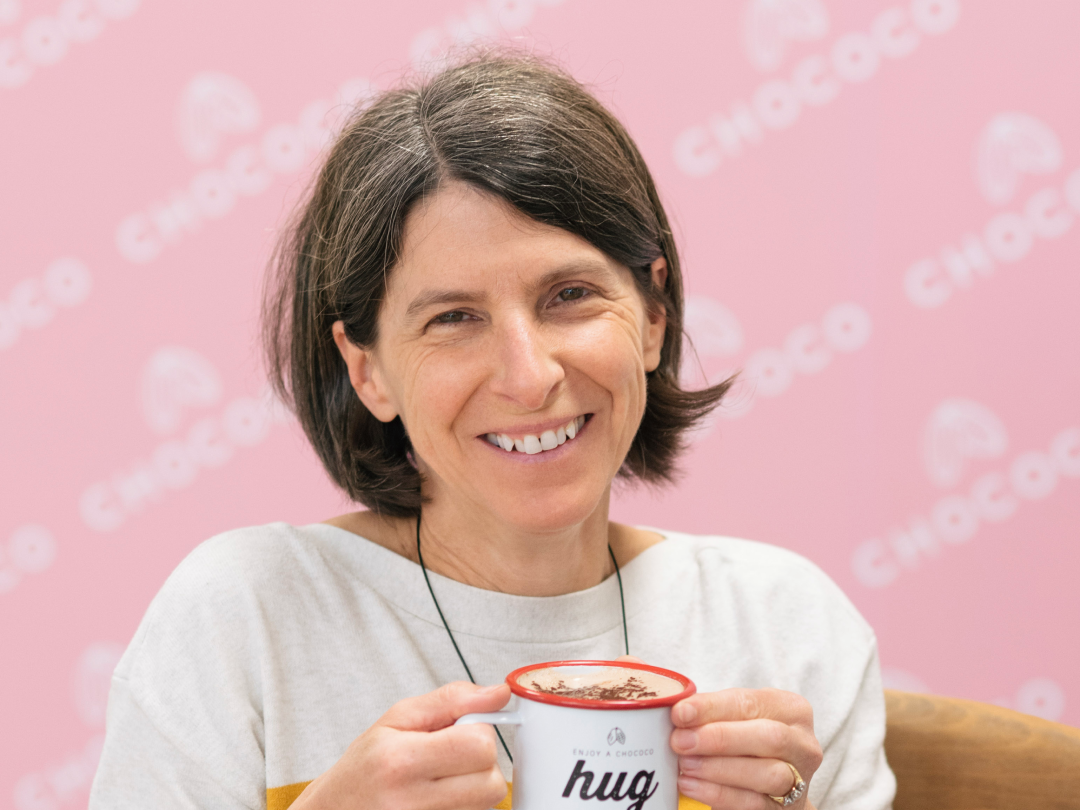 Smiling woman holding a mug of hot chocolate with a pink Chococo background
