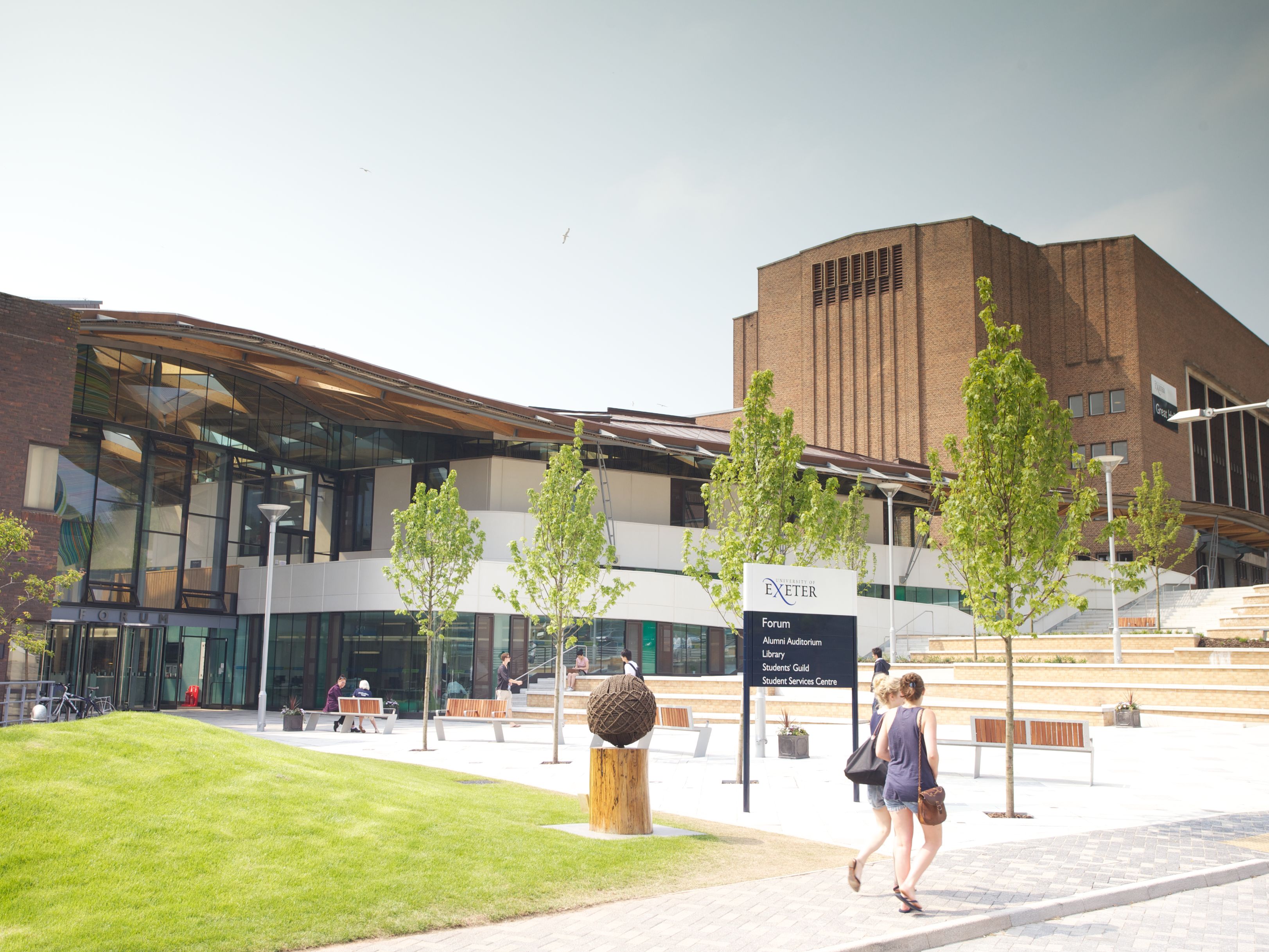 Modern university campus area with students walking and a sign for the Forum at the University of Exeter.