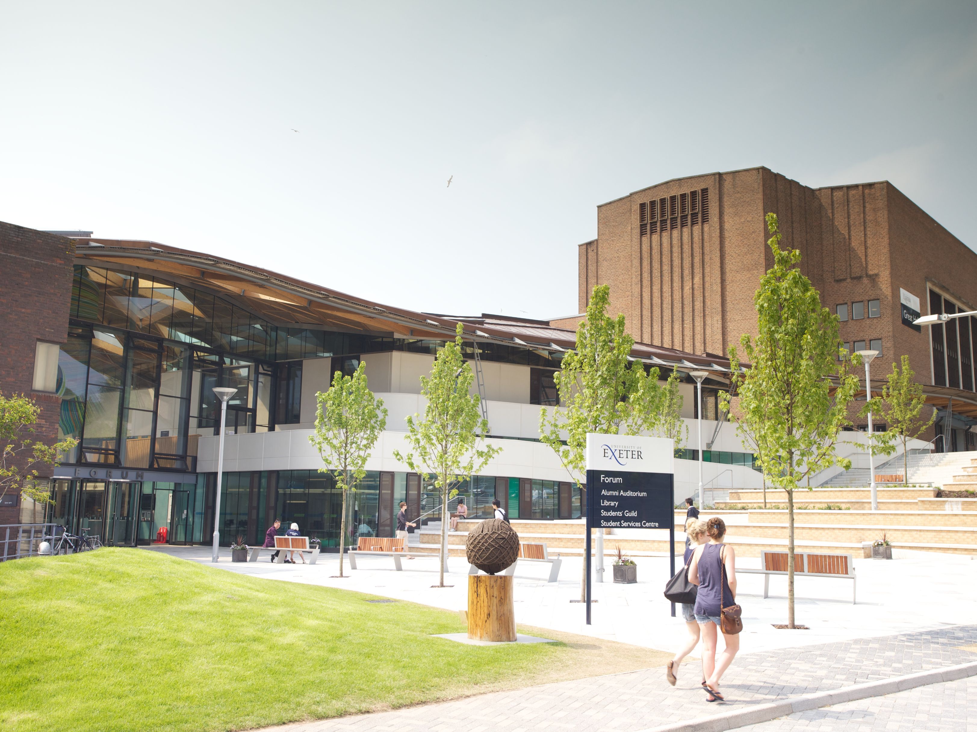 Modern university campus area with students walking and a sign for the Forum at the University of Exeter.
