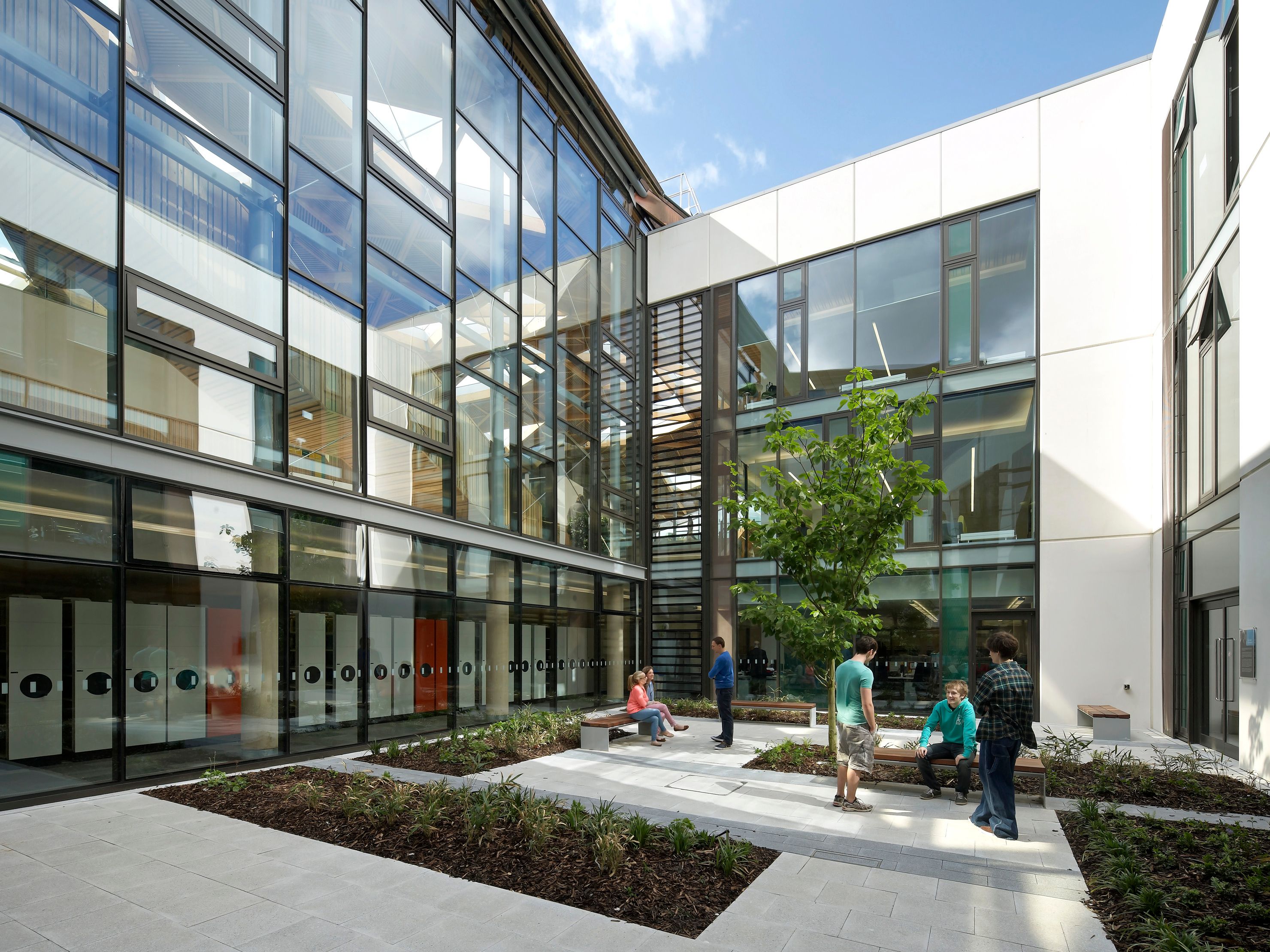 Modern building courtyard with glass walls and people talking and sitting on benches