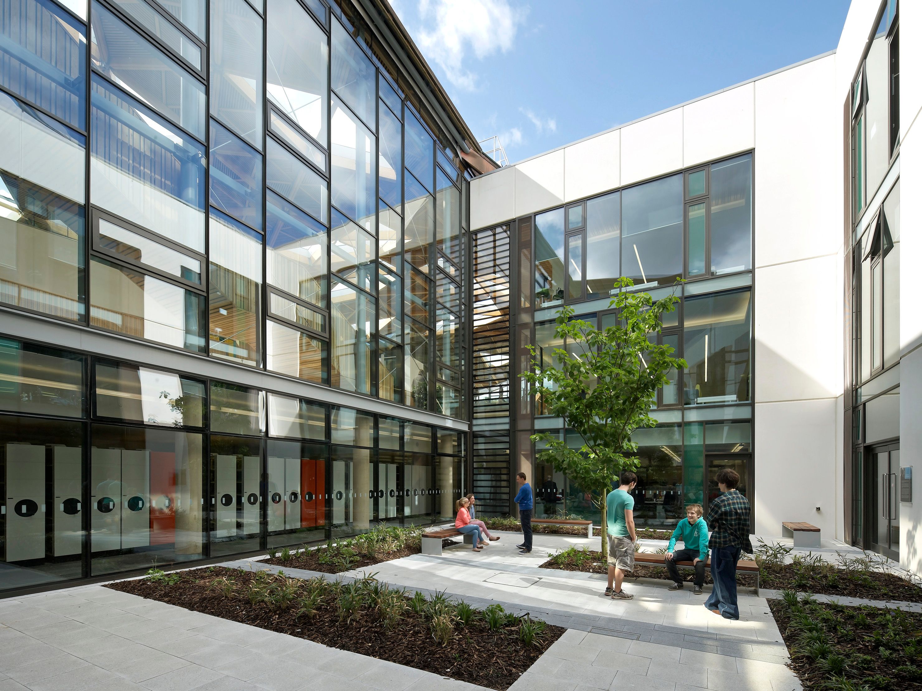 Modern building courtyard with glass walls and people talking and sitting on benches