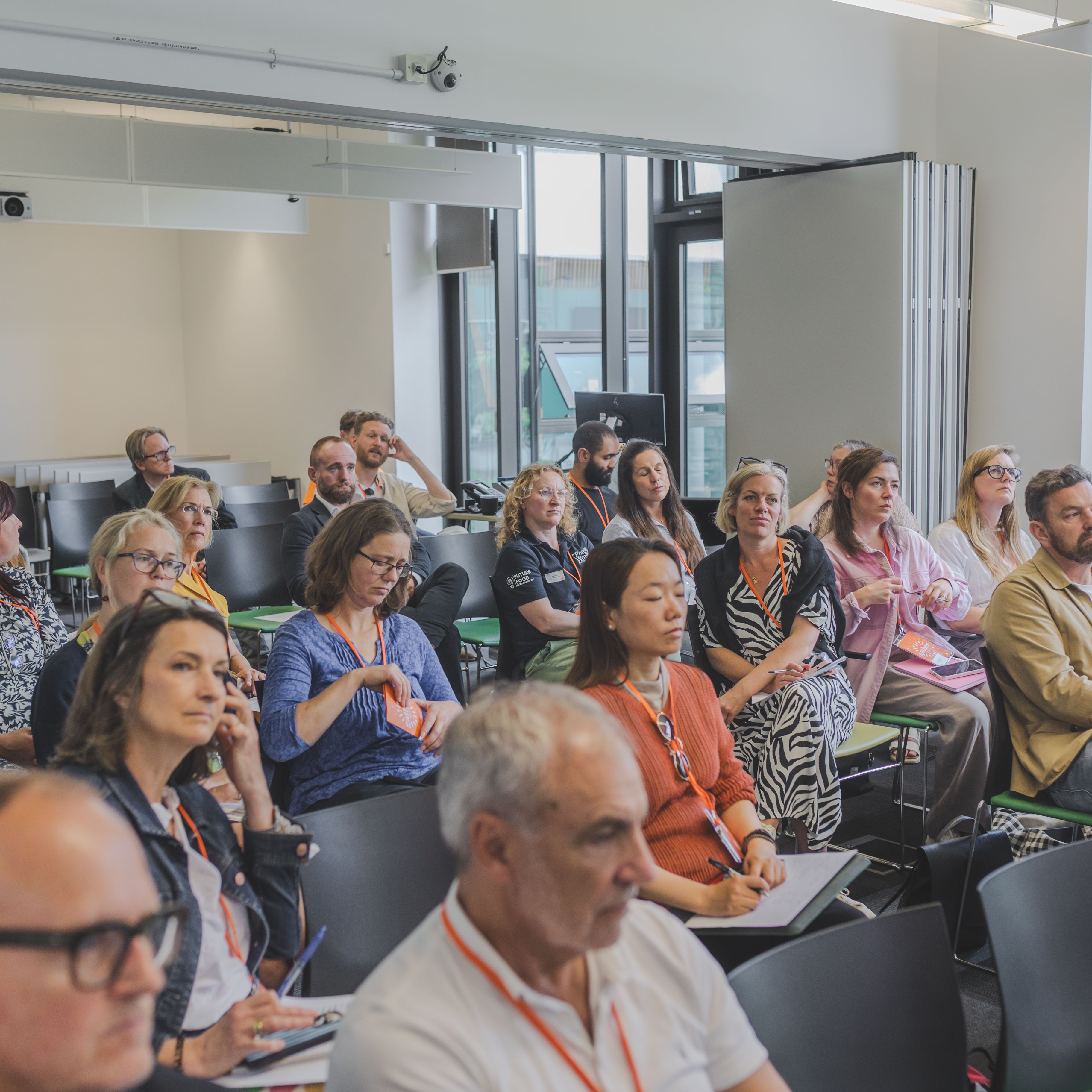 A group of adults attentively listening during a seminar or workshop in a modern classroom setting.