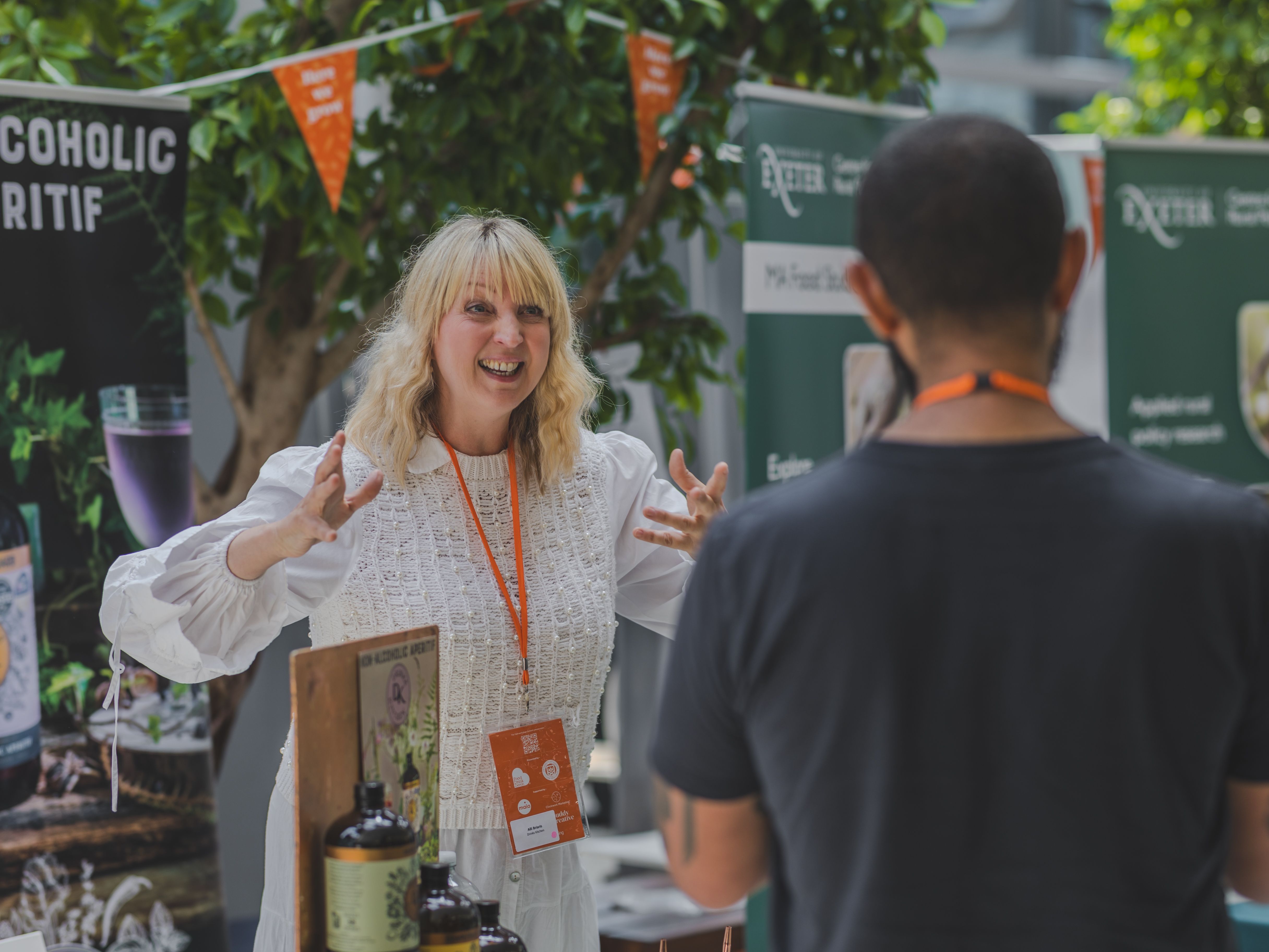 Woman enthusiastically talking to a visitor at a booth for non-alcoholic aperitifs during an event.