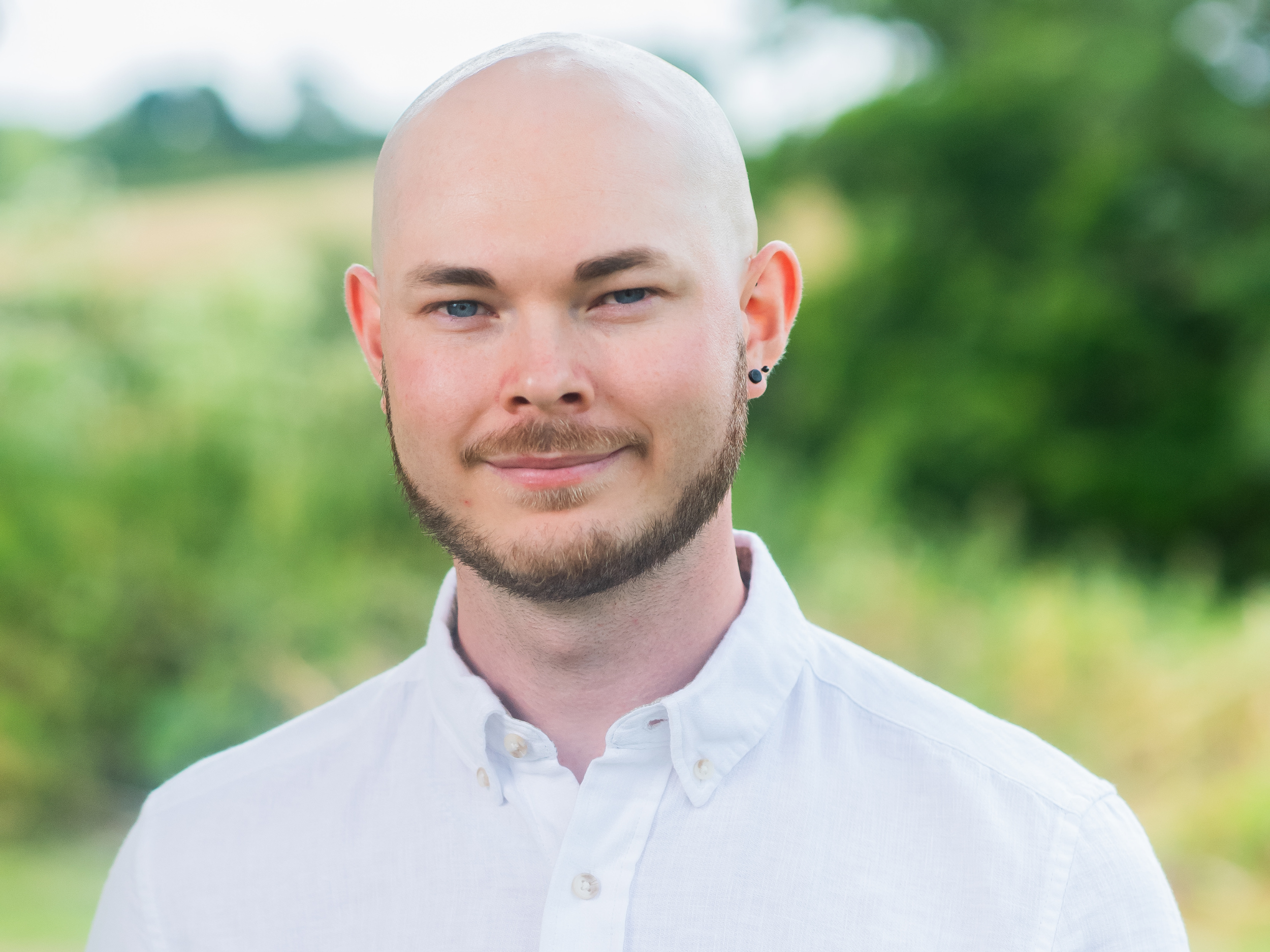 Bald man with a beard wearing a white button-up shirt standing outdoors.