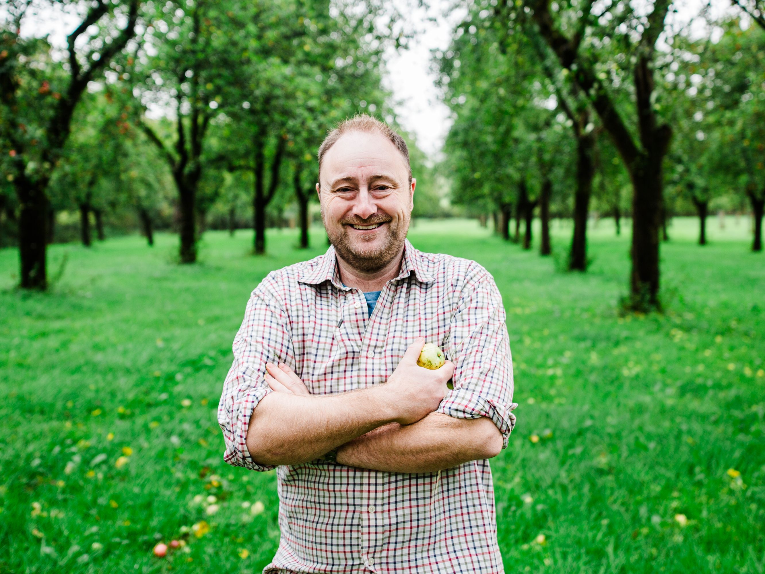 Smiling man standing in an orchard holding an apple