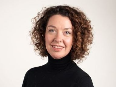 Woman with curly brown hair wearing a black turtleneck sweater, smiling at the camera.