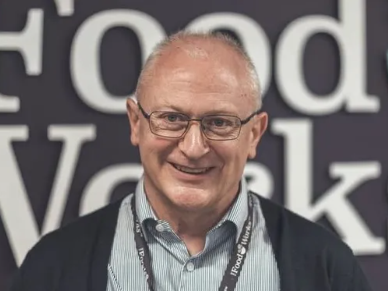 Smiling older man wearing glasses, standing in front of a sign that says 'Food Works'