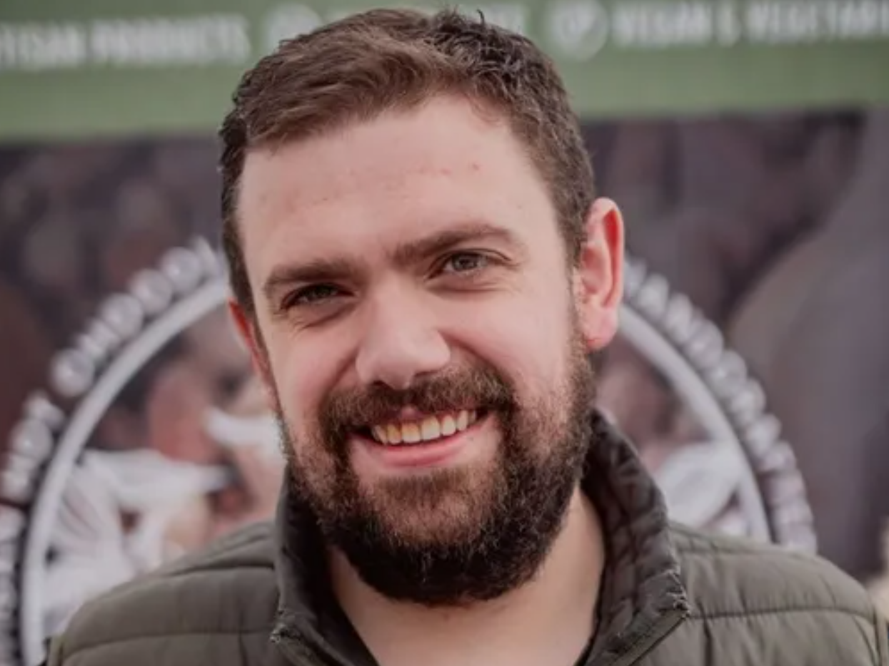 Smiling man with a beard standing outdoors in front of a blurred background