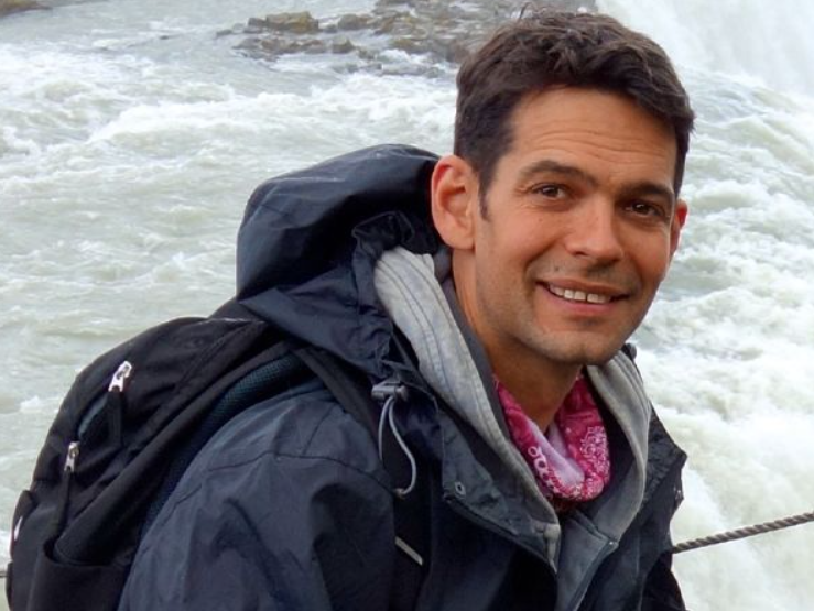 Man in outdoor gear smiling near a river or waterfall