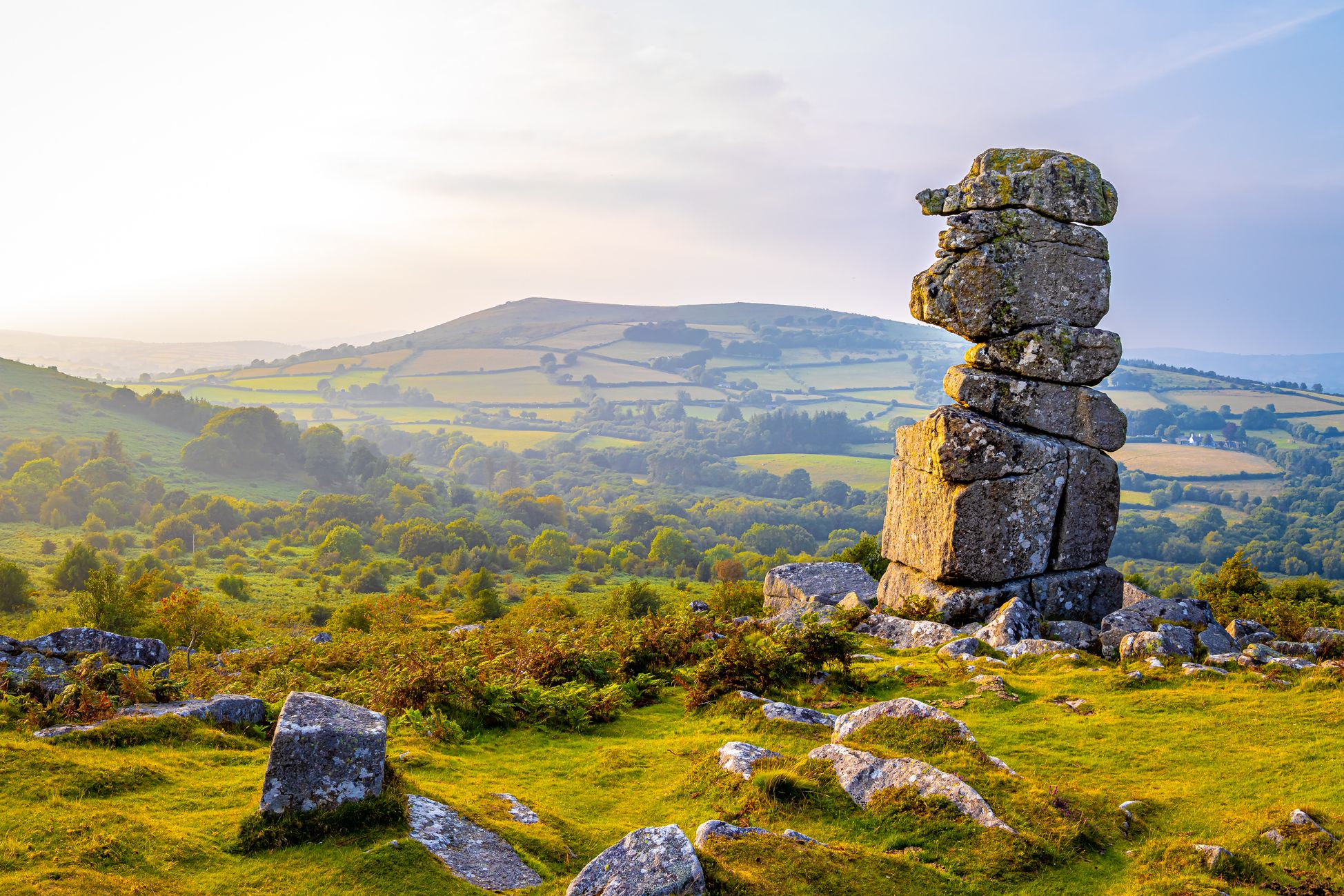 Bowermans Nose stands prominently in a lush, rolling landscape under soft morning or evening light. Green fields, trees, and distant hills add depth to the serene countryside view.